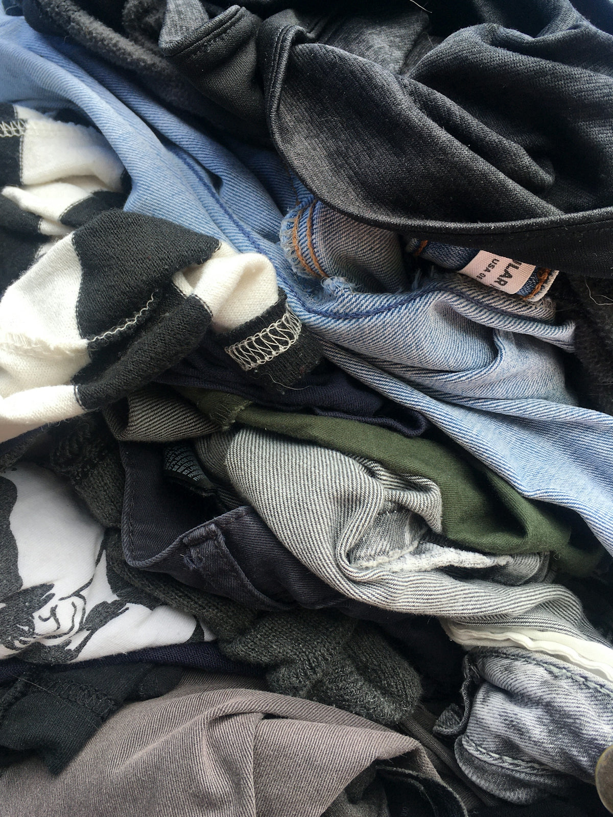 A pile of assorted clothing including denim jeans and black and white shirts