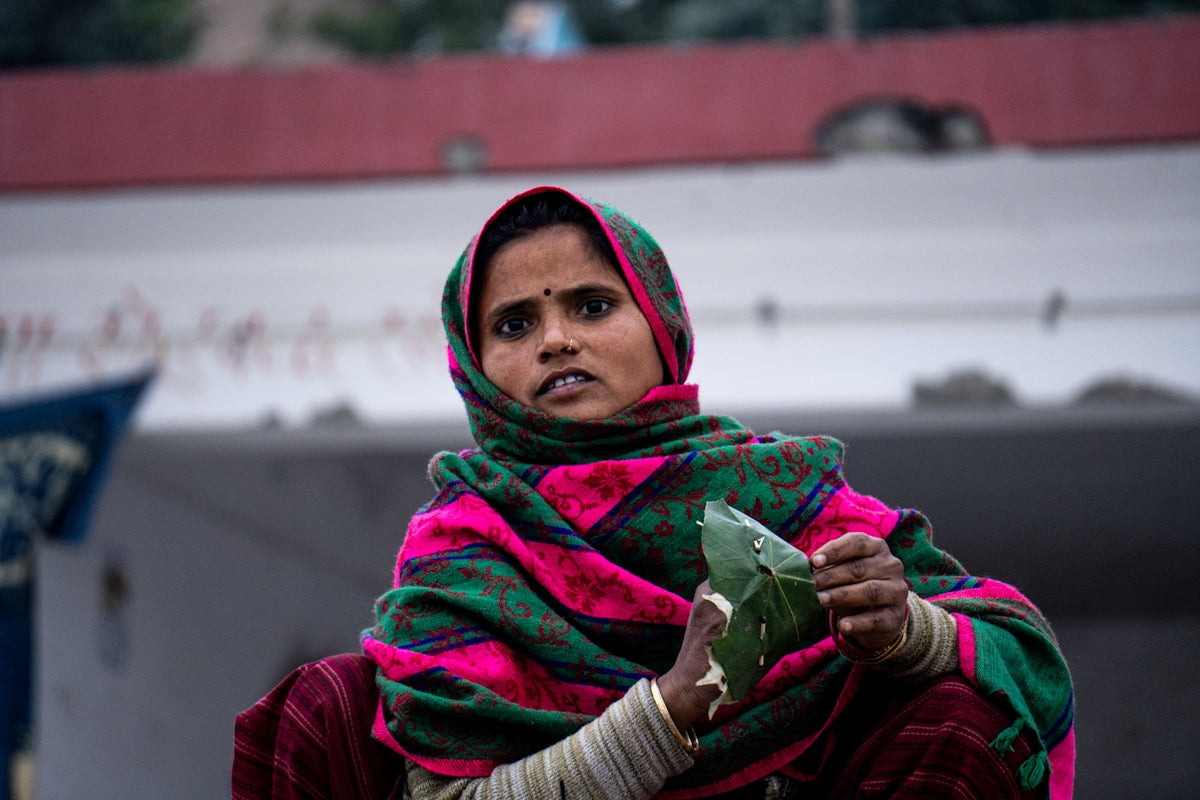 A woman in a colorful headscarf holds green leaves.