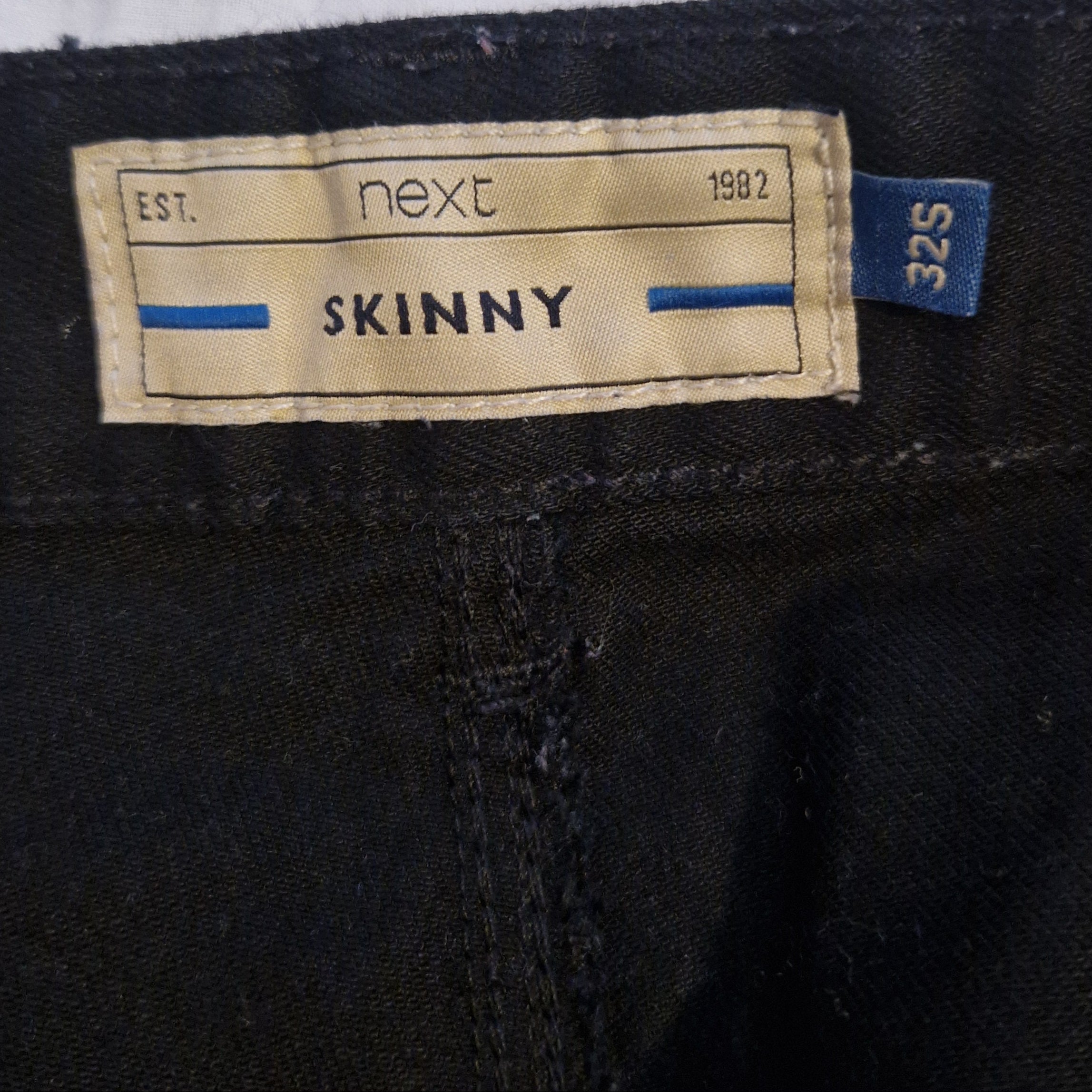 A close-up of a black Next skinny fit jeans label showing a size 32 waist and short length.