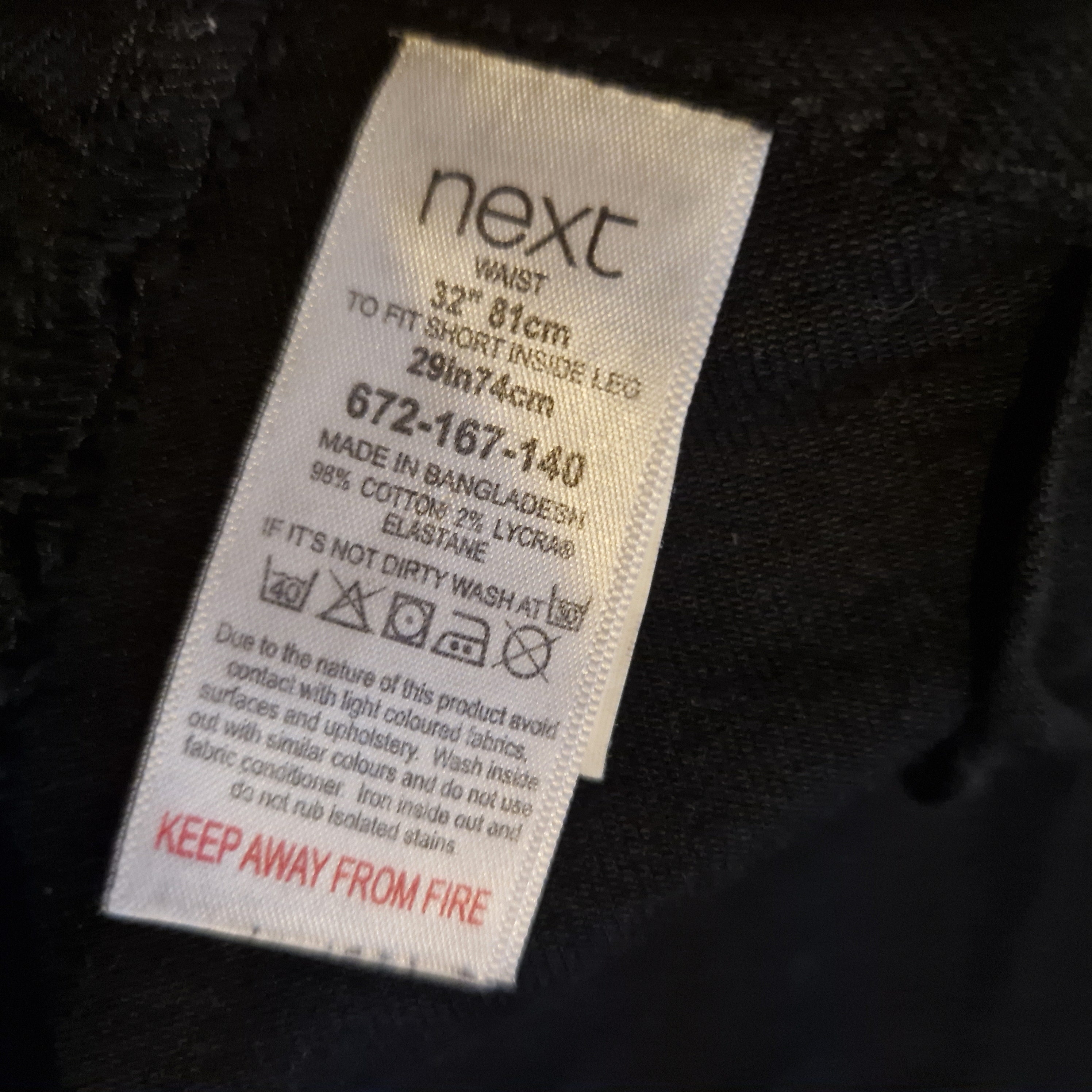 A close-up of a Next clothing label inside black skinny fit jeans with a 32 inch waist.
