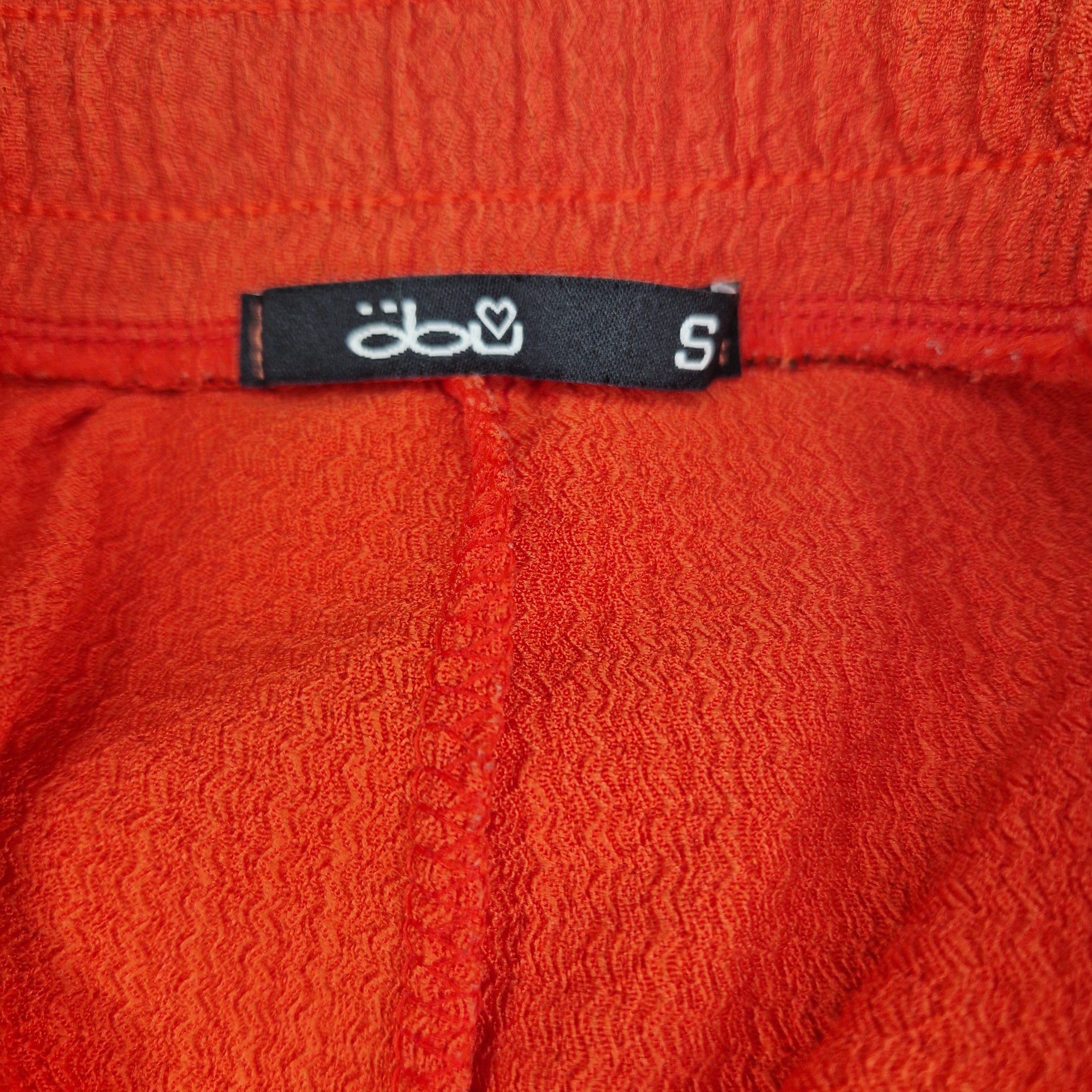 Close-up of the black brand label and size small tag on red wide-leg trousers.