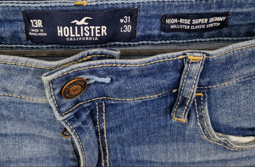 A close-up of the waistband and button closure on blue Hollister high-rise super skinny jeans.