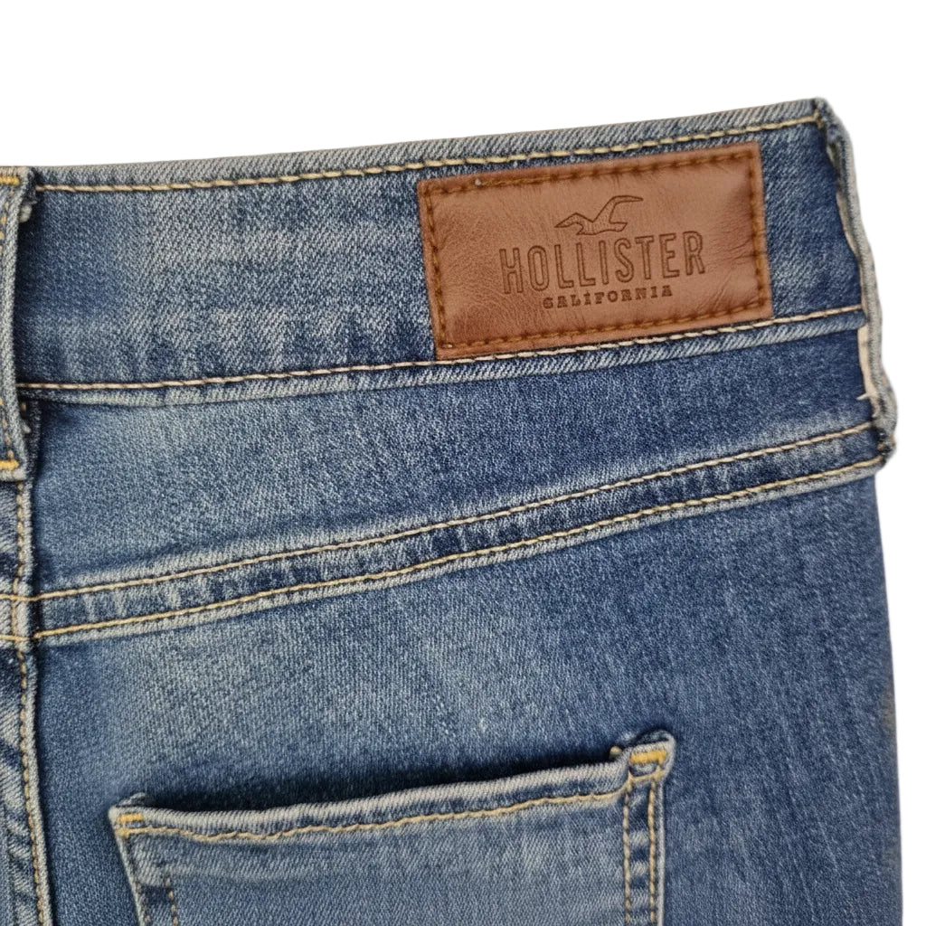 A close-up of the back waistband and pocket of medium blue Hollister denim jeans.