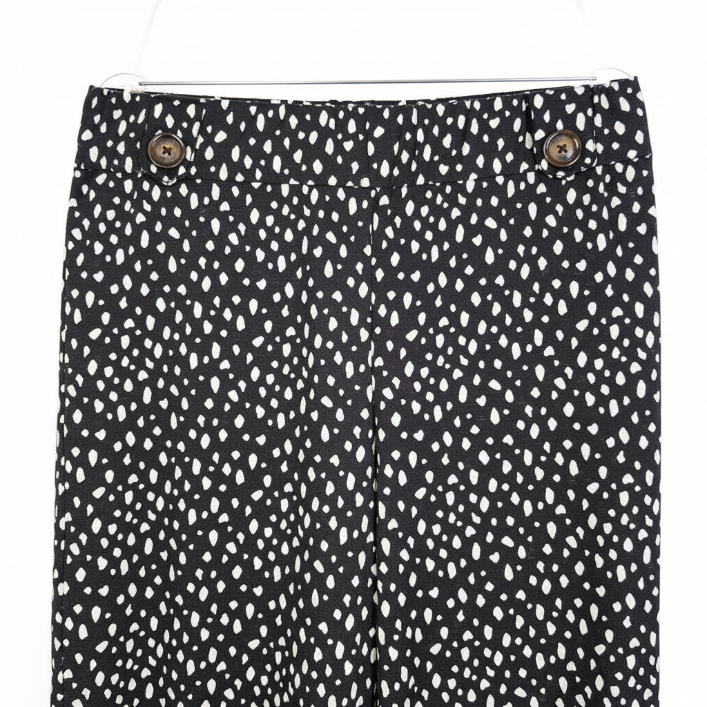 Black tapered trousers with a white abstract print, featuring an elasticated waist and button detail.