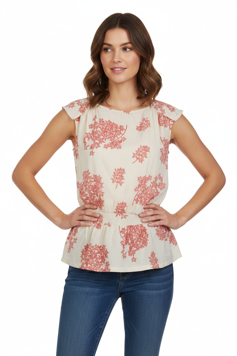 A sleeveless cream blouse with a pink floral print and a smocked hem worn with blue jeans.
