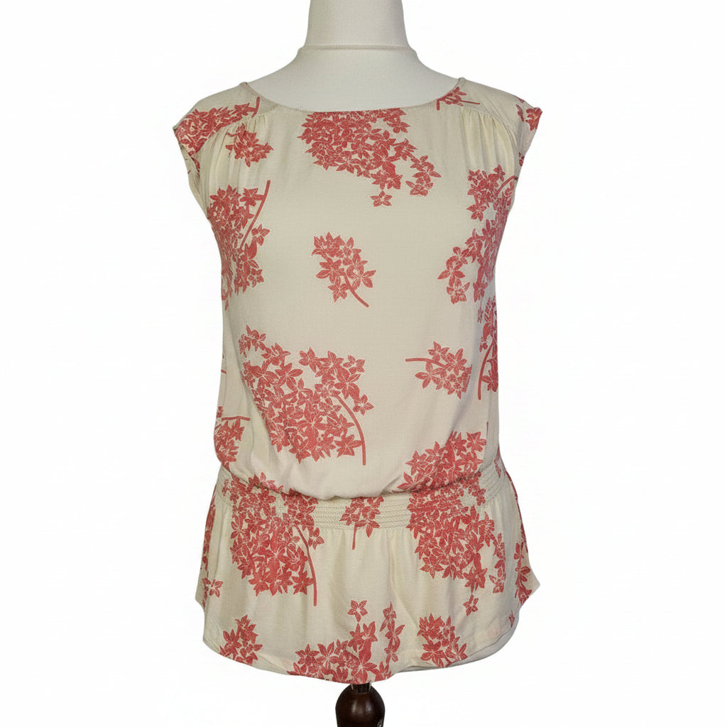 A sleeveless cream blouse with a pink floral print and a smocked hem.