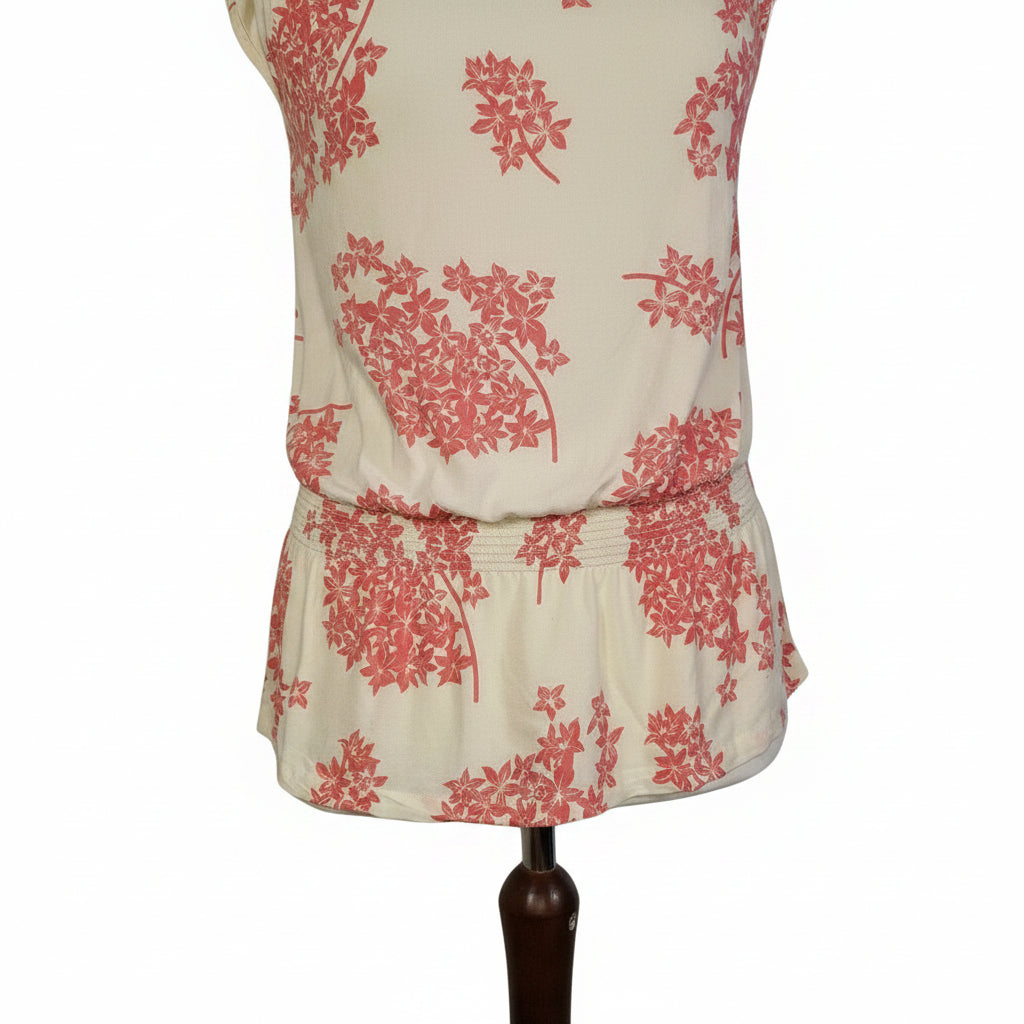 A sleeveless cream blouse with a pink floral print and a smocked hem.