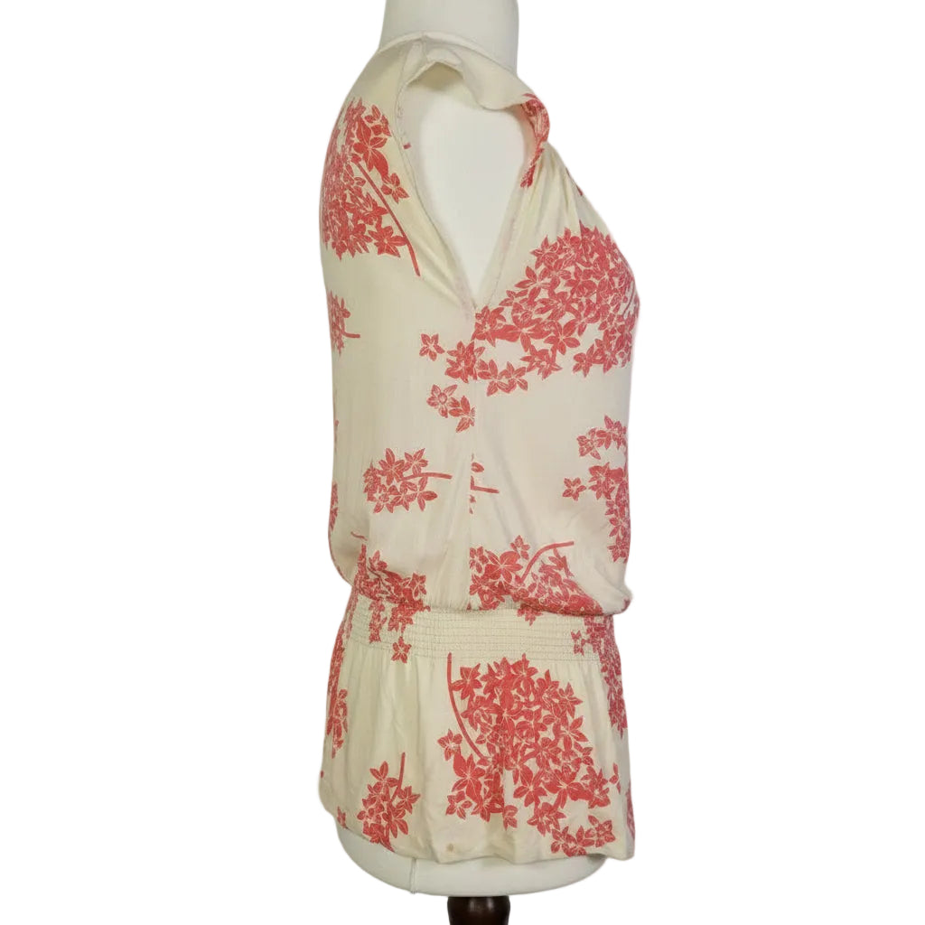 A sleeveless cream blouse with a pink floral print and a smocked hem.