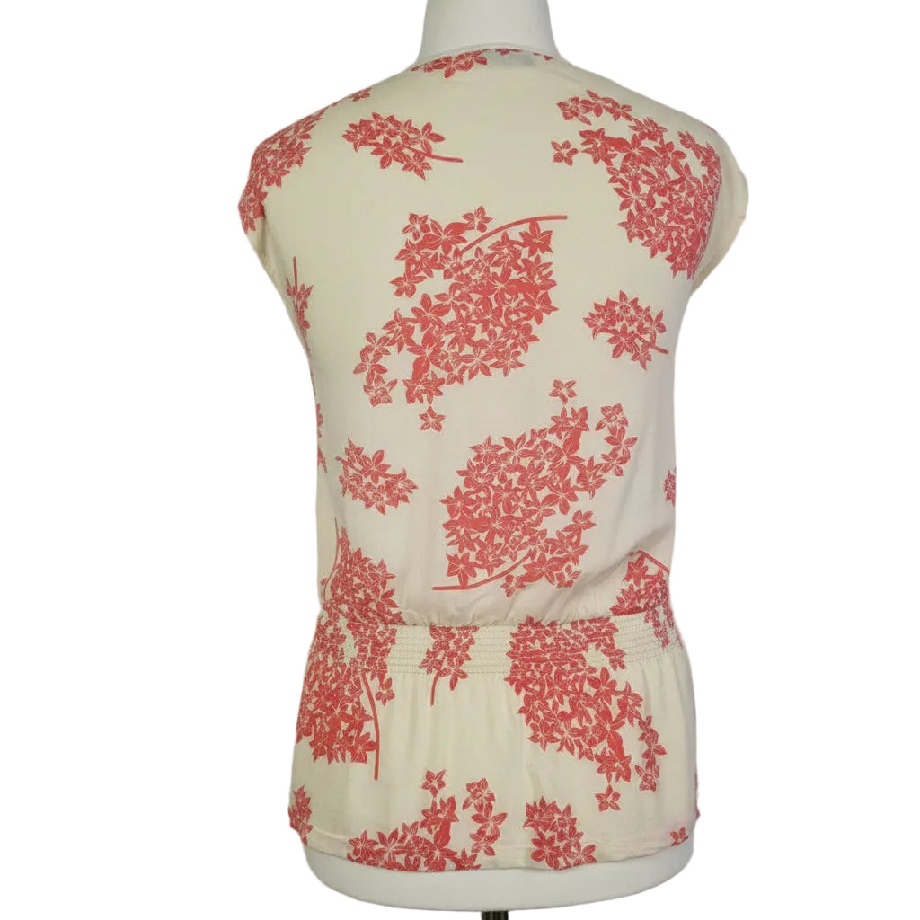 A sleeveless cream blouse with a pink floral print and a smocked hem.