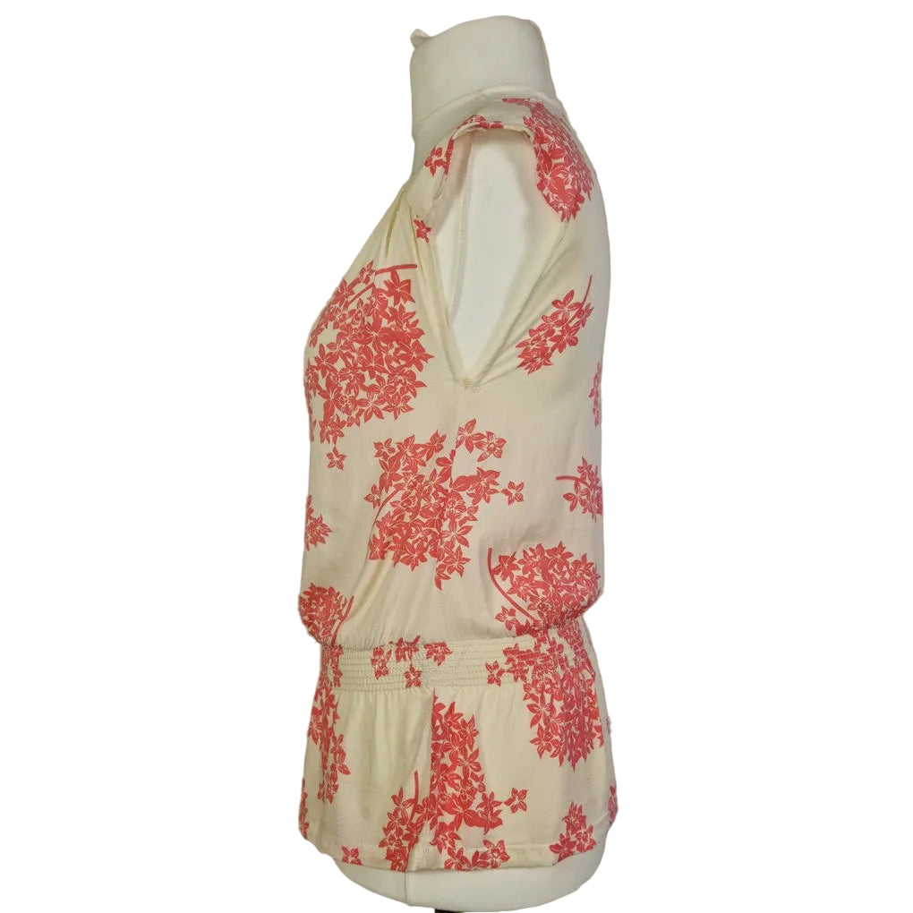 A sleeveless cream blouse with a pink floral print and a smocked hem on a mannequin.