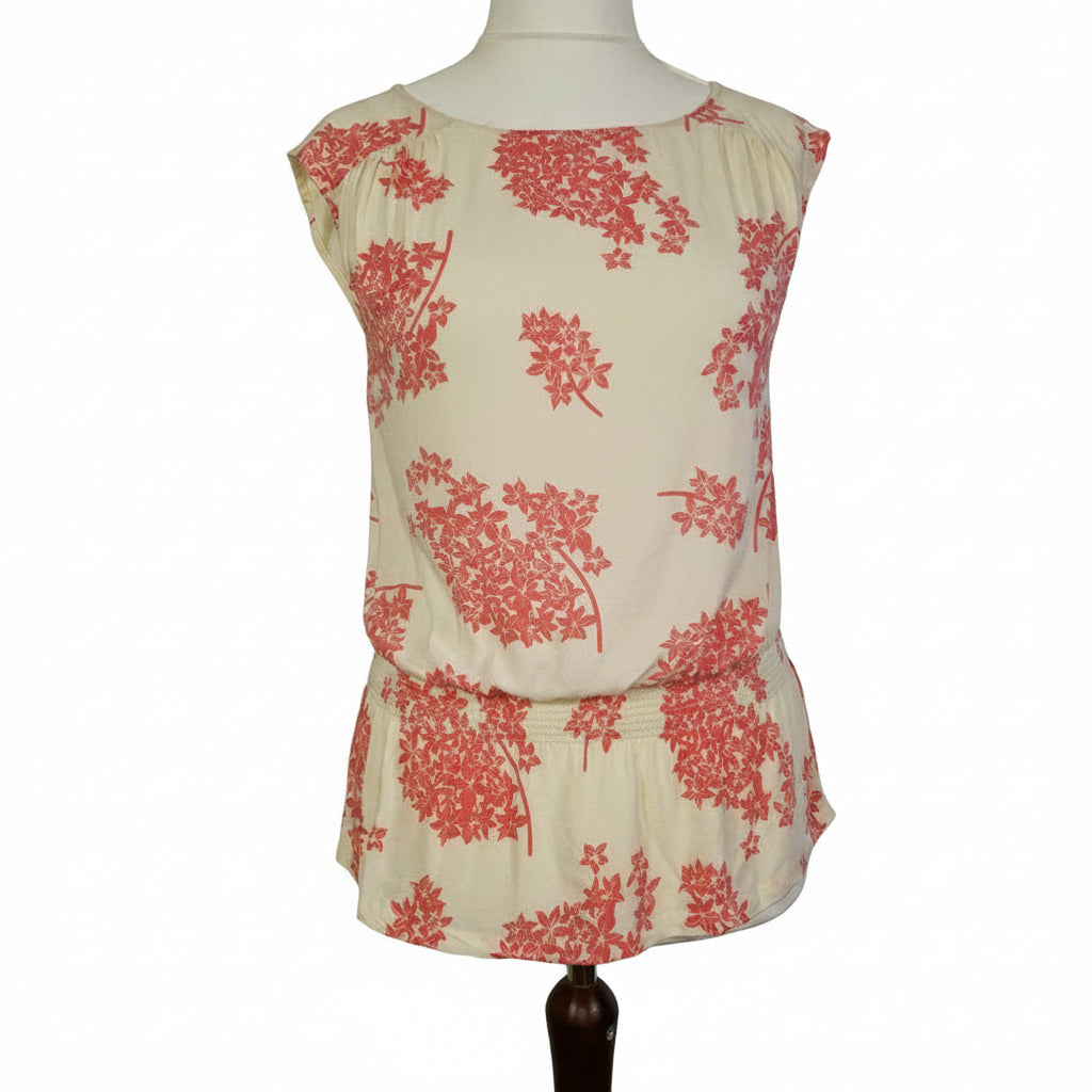 A sleeveless cream blouse by F&F featuring a pink floral print and a smocked hem.