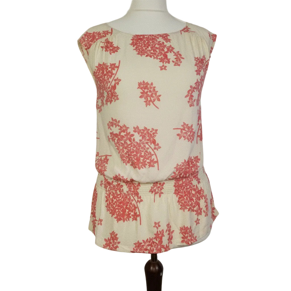A sleeveless cream blouse with a pink floral print and a smocked hem on a mannequin.