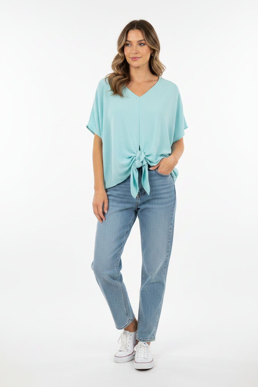 A woman wears a light blue V-neck blouse with a tie-front detail and short sleeves.