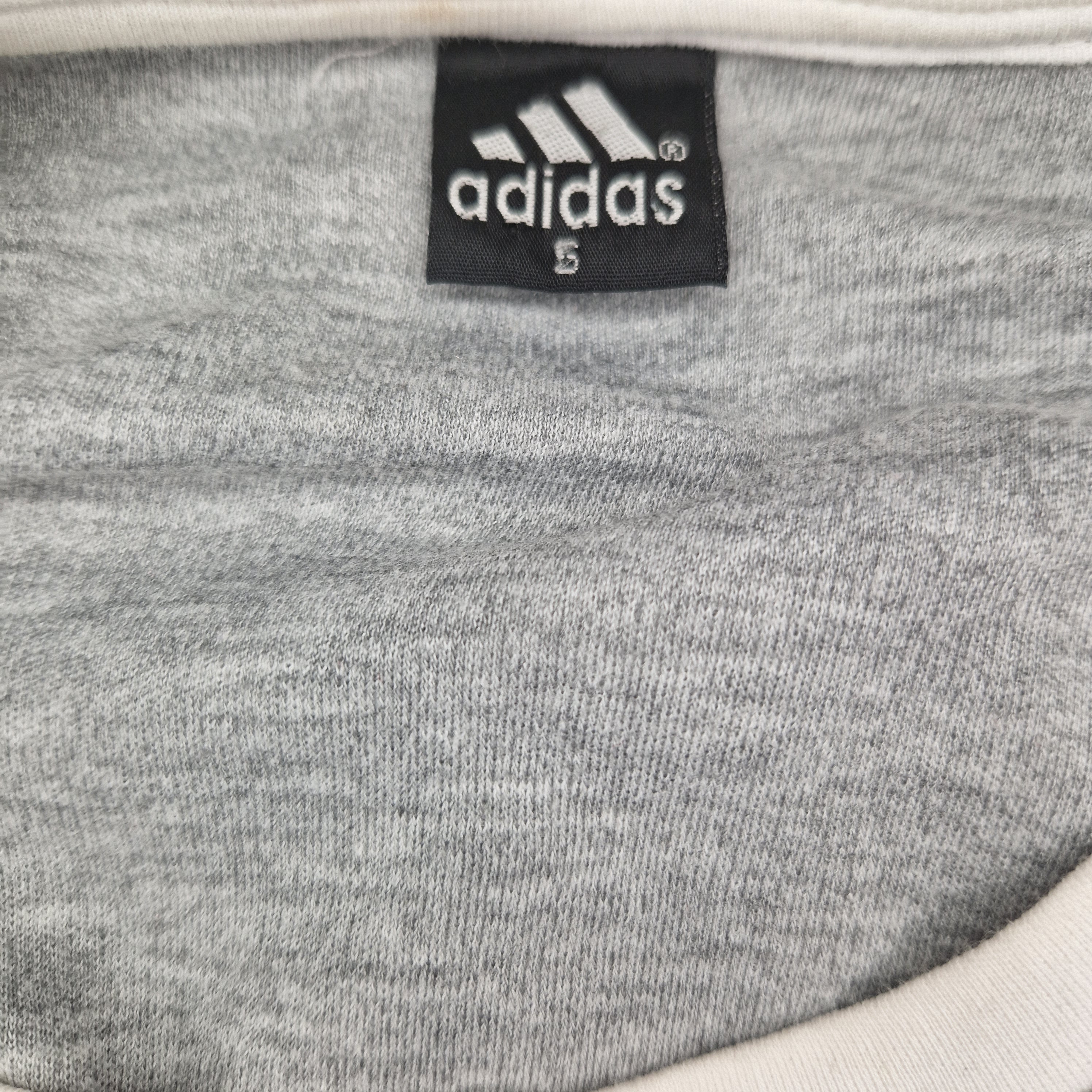 A close-up view of the interior neck label on a grey Adidas women's cotton t-shirt in size small.