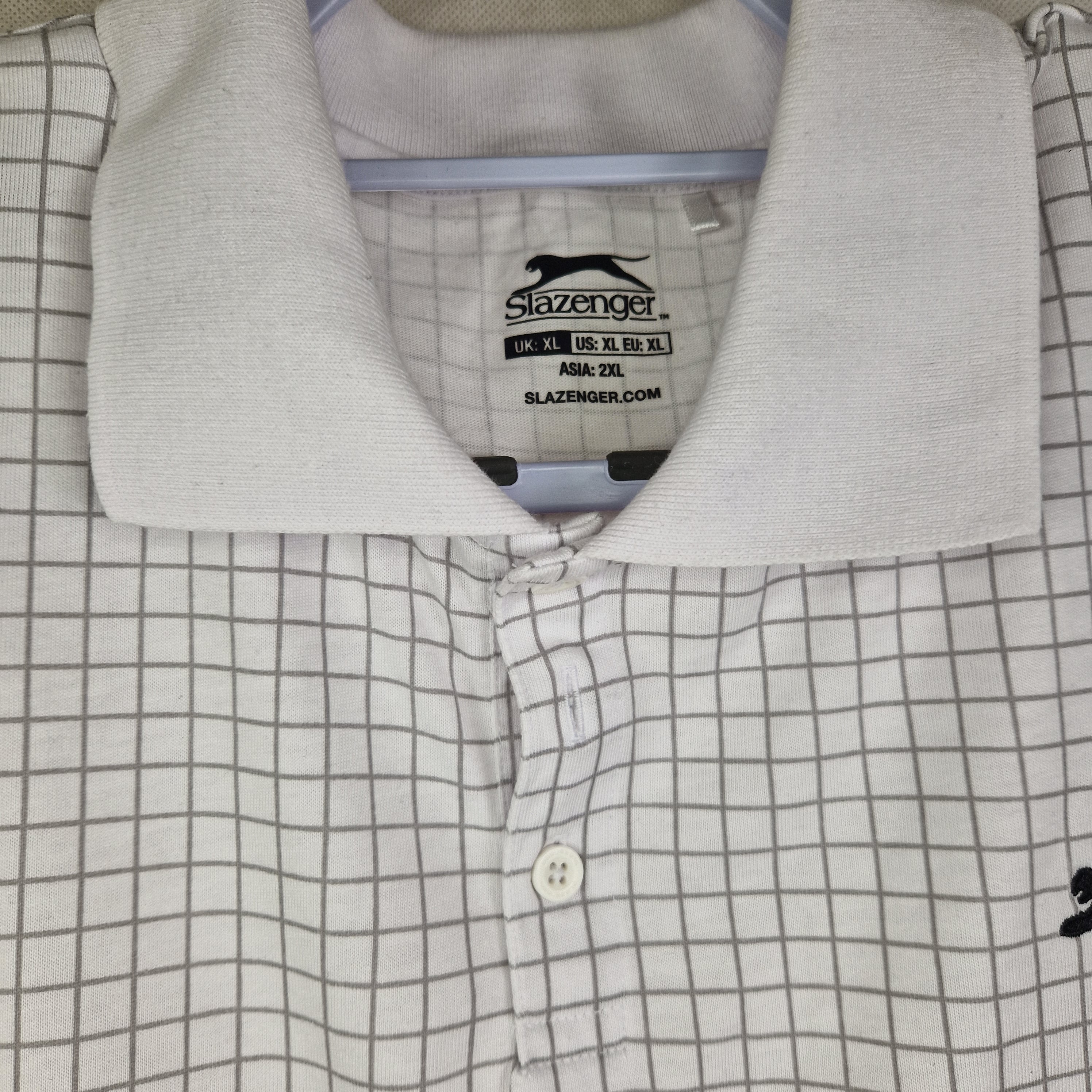 A white Slazenger polo shirt featuring a grey grid check pattern and a collared neckline.