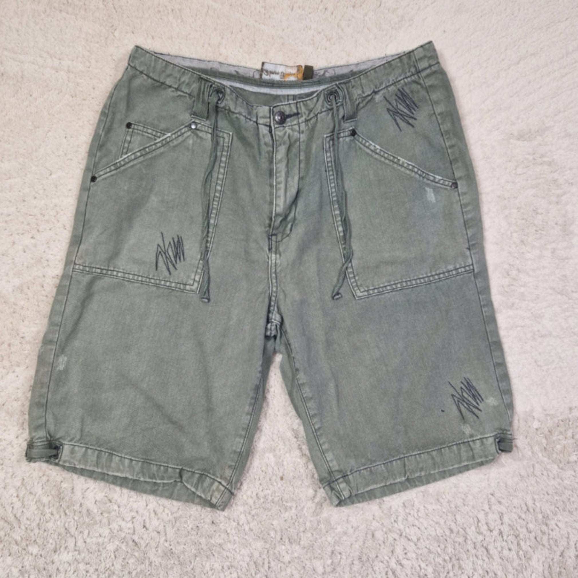 Green denim shorts with branding on a light gray carpet
