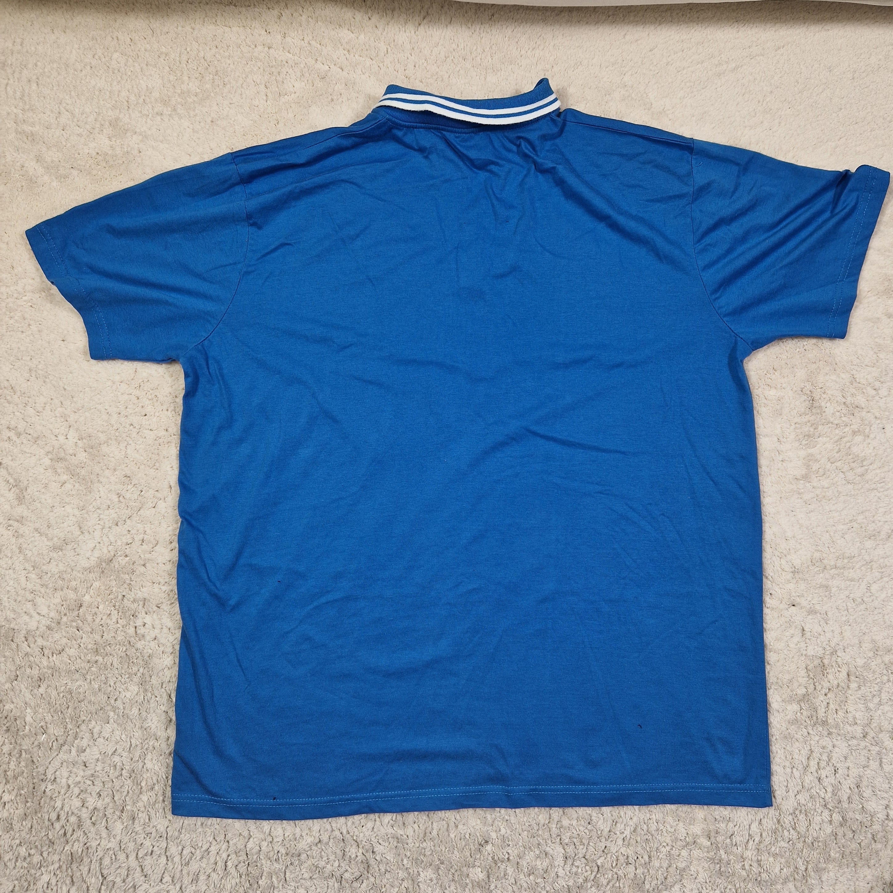 Blue t-shirt with white stripes on sleeves laid flat on a beige carpet