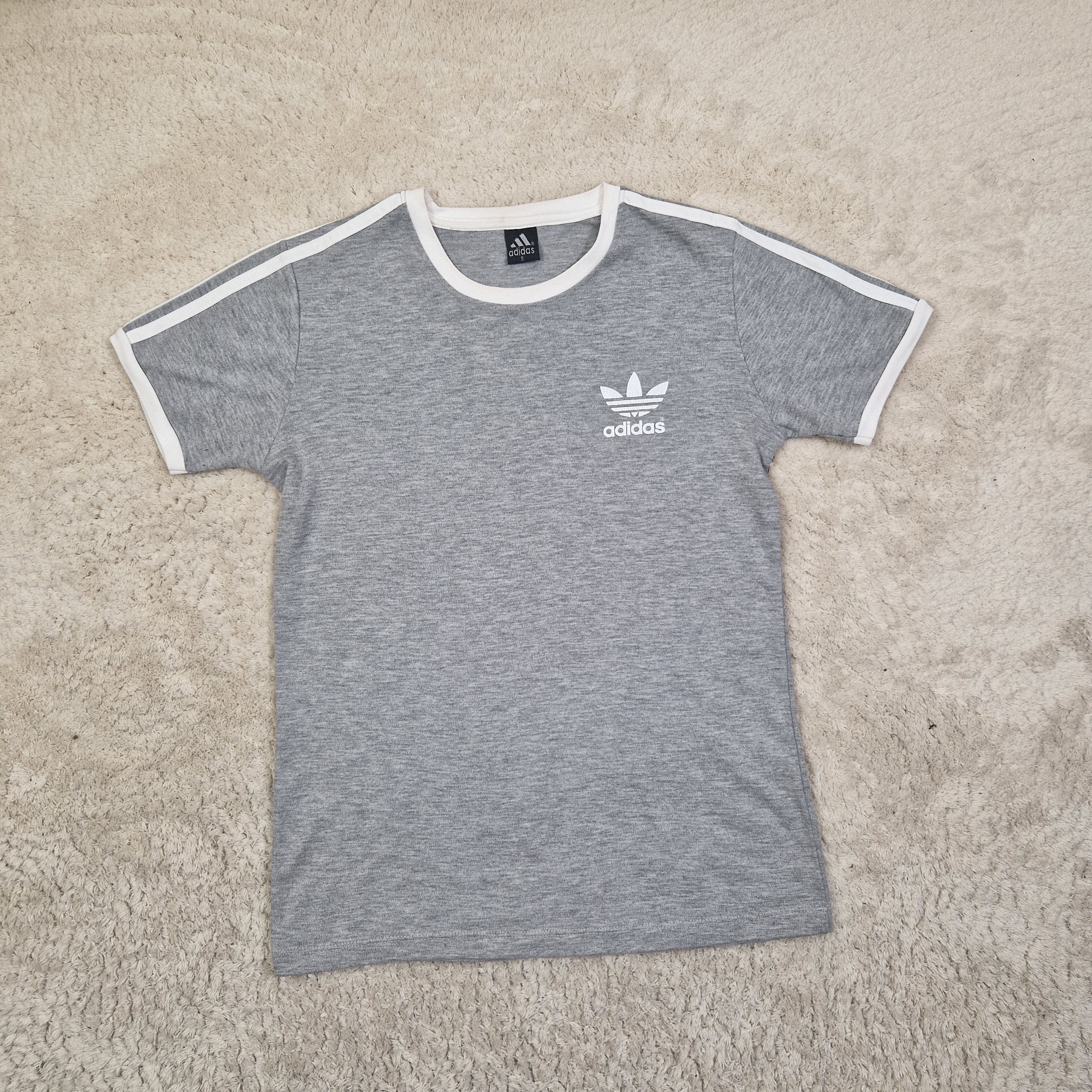 Gray t-shirt with white trim and Adidas logo on a beige carpet