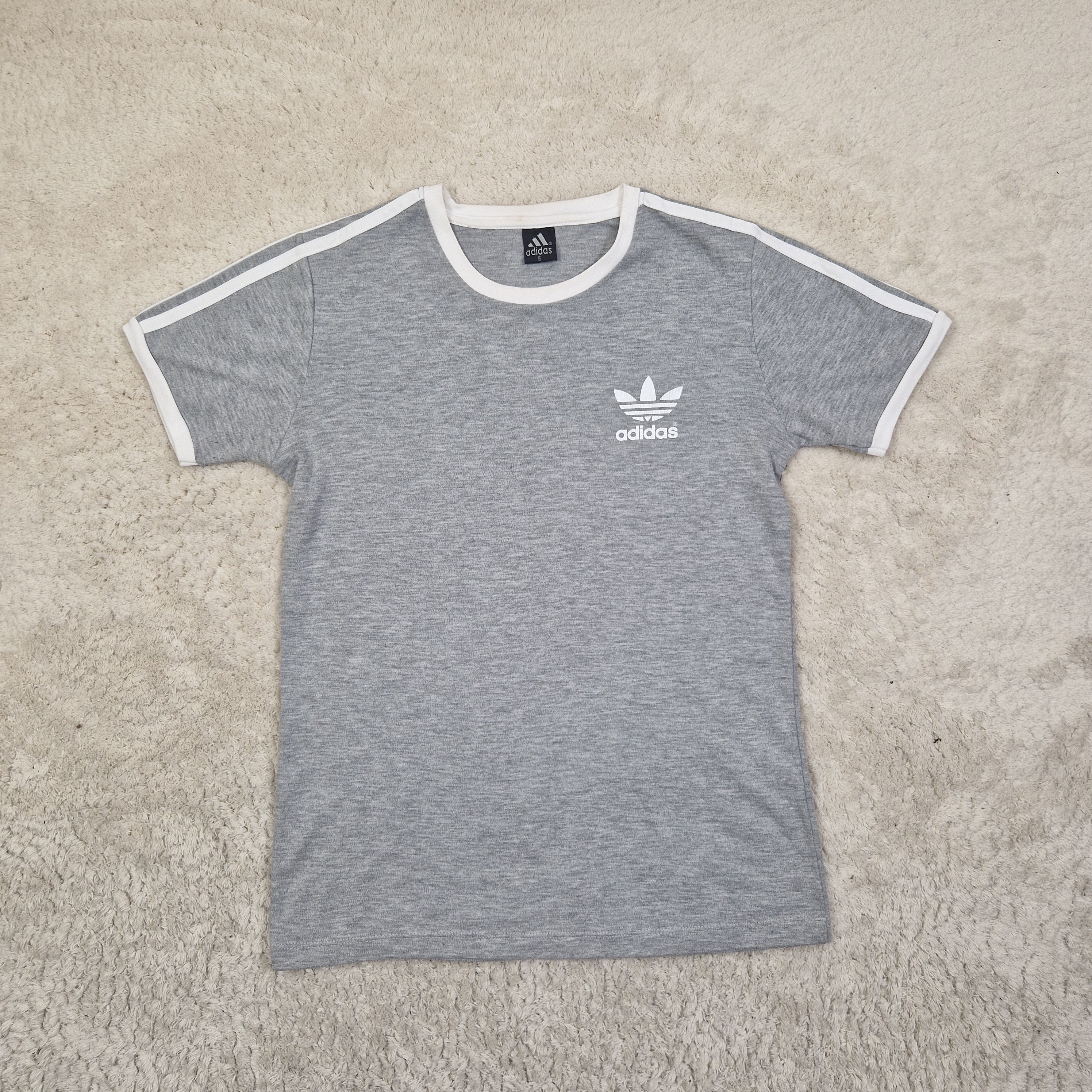 Gray t-shirt with Adidas logo on a beige carpet