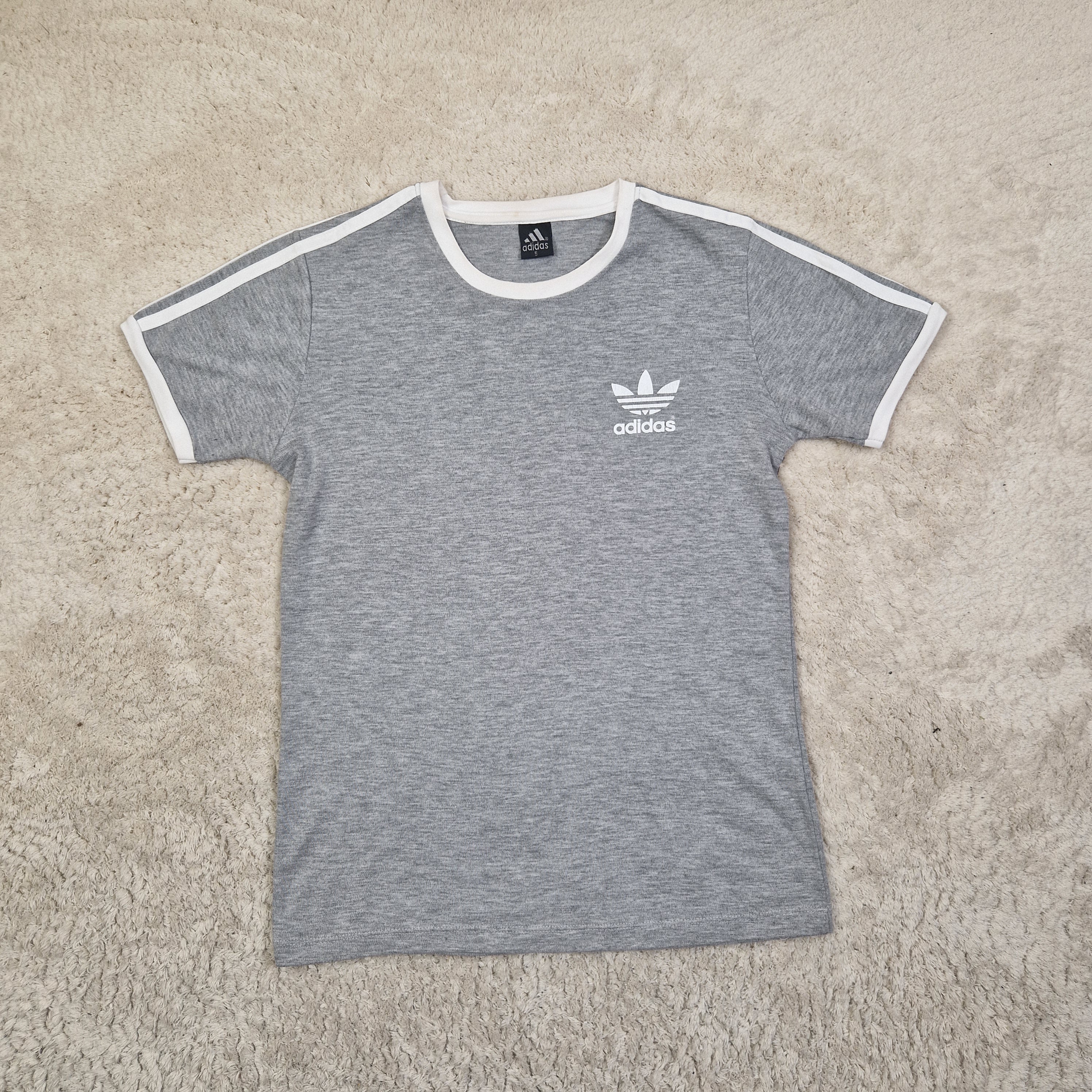 Gray t-shirt with Adidas logo on a beige carpet