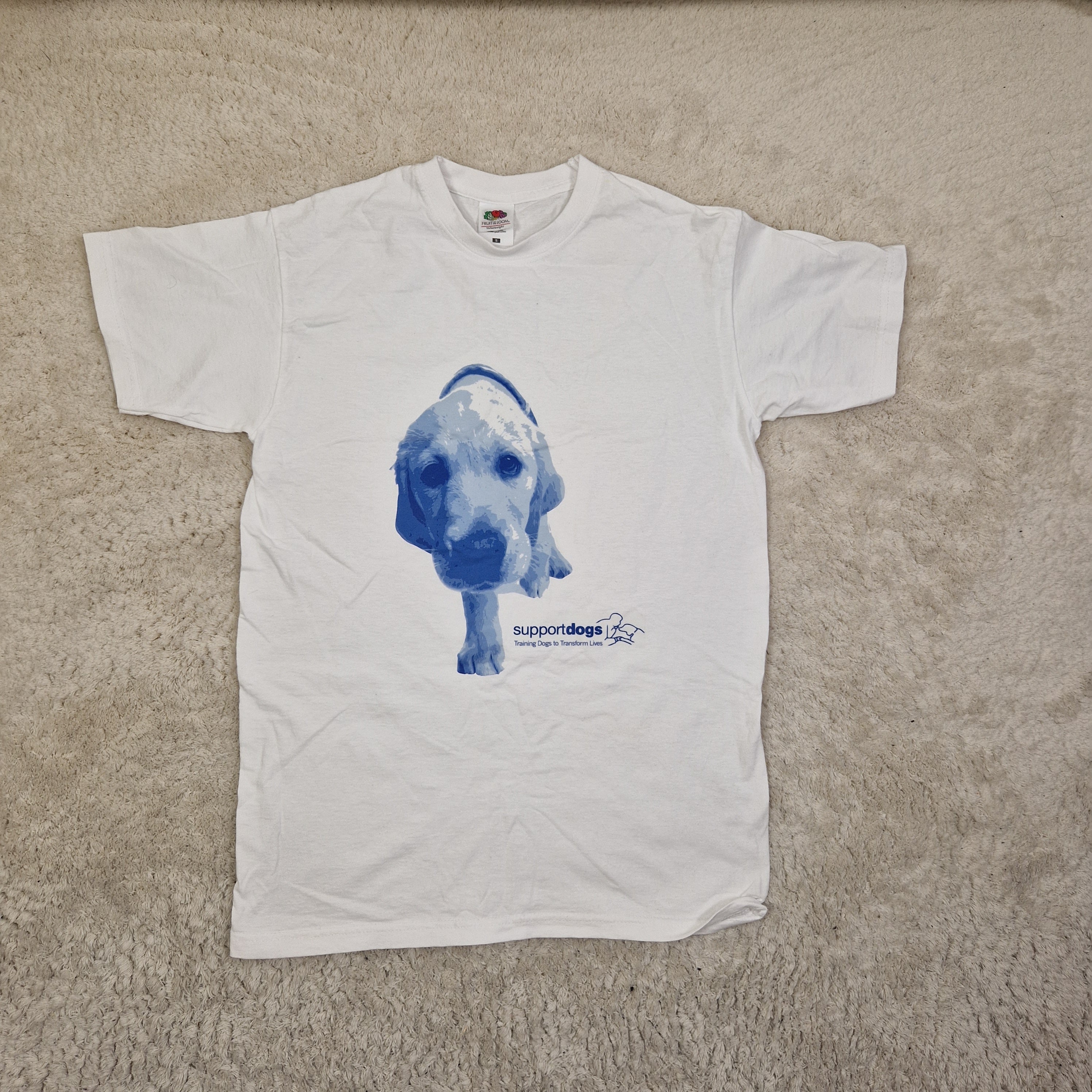 White t-shirt with a blue graphic of a dog on a beige carpet