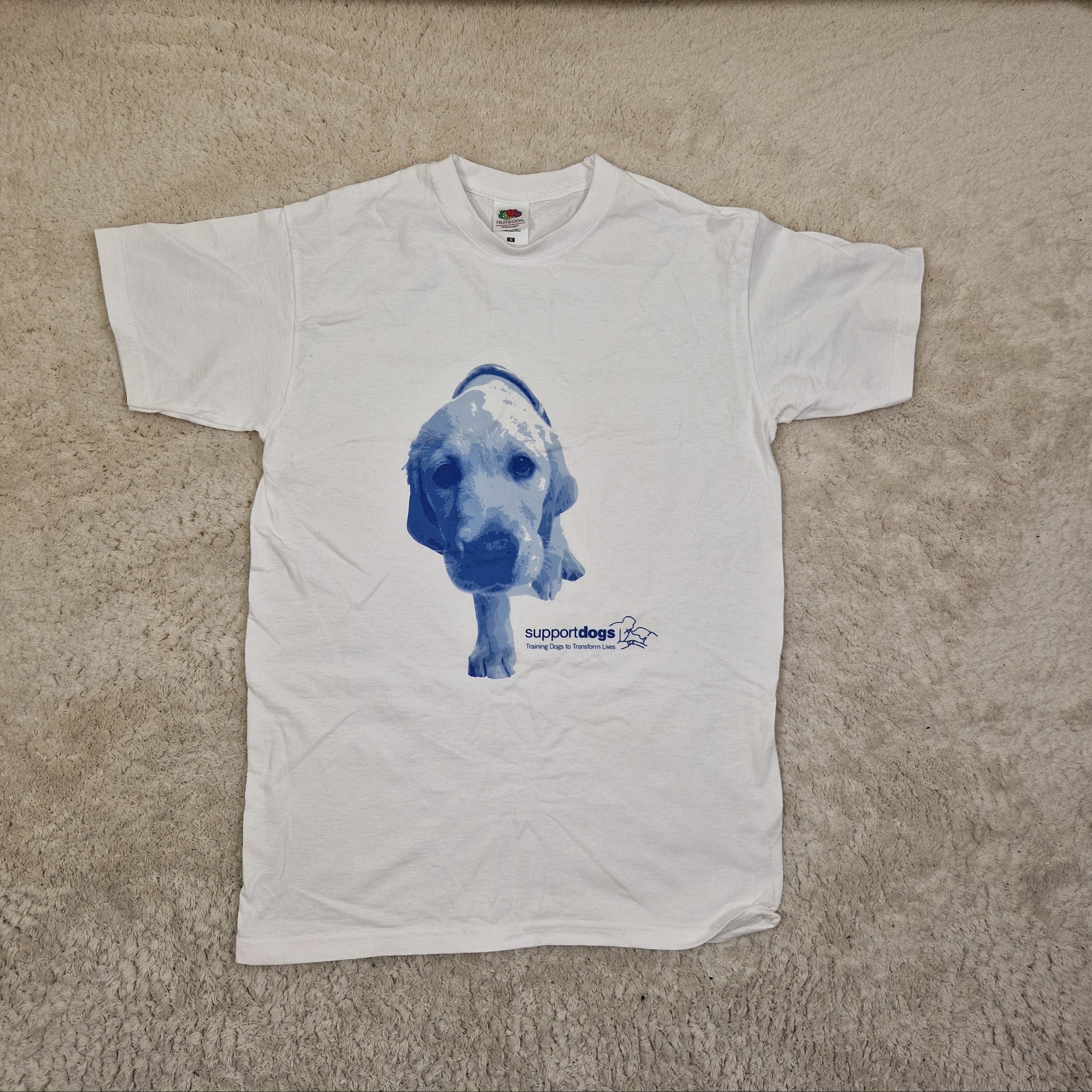 White t-shirt with blue graphic design on a beige carpet