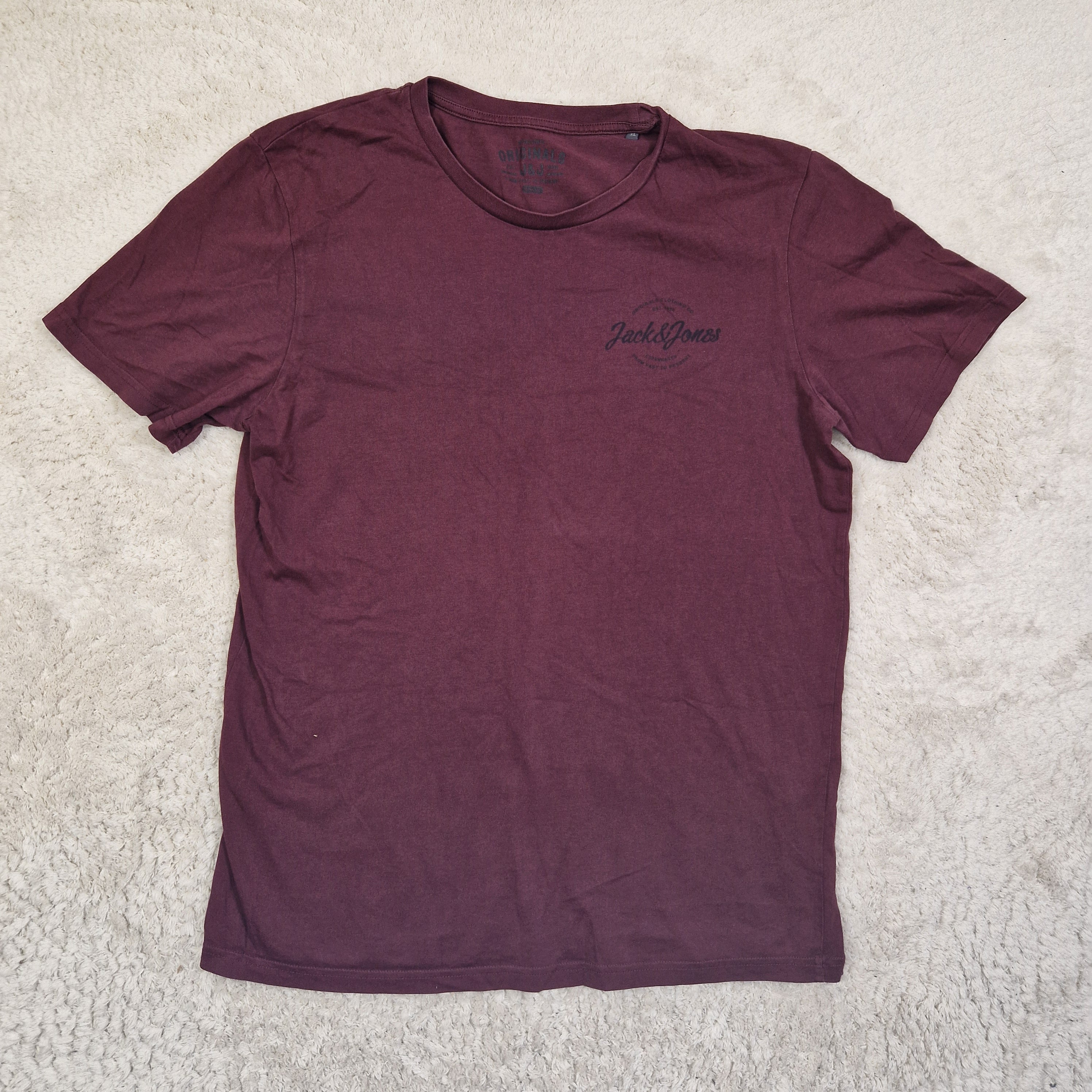 Maroon t-shirt with a logo on a beige carpet
