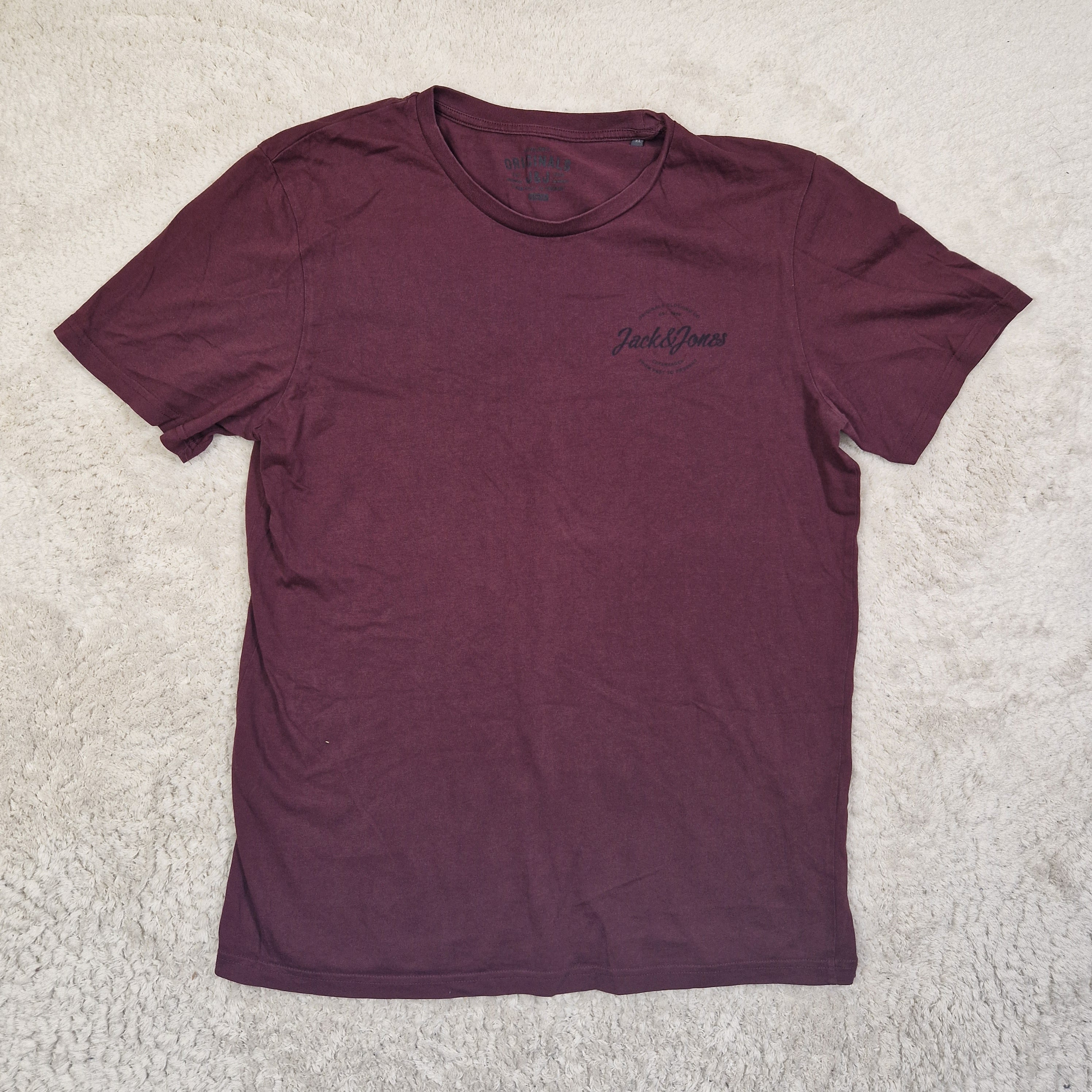 Maroon t-shirt with a logo on a light gray carpet