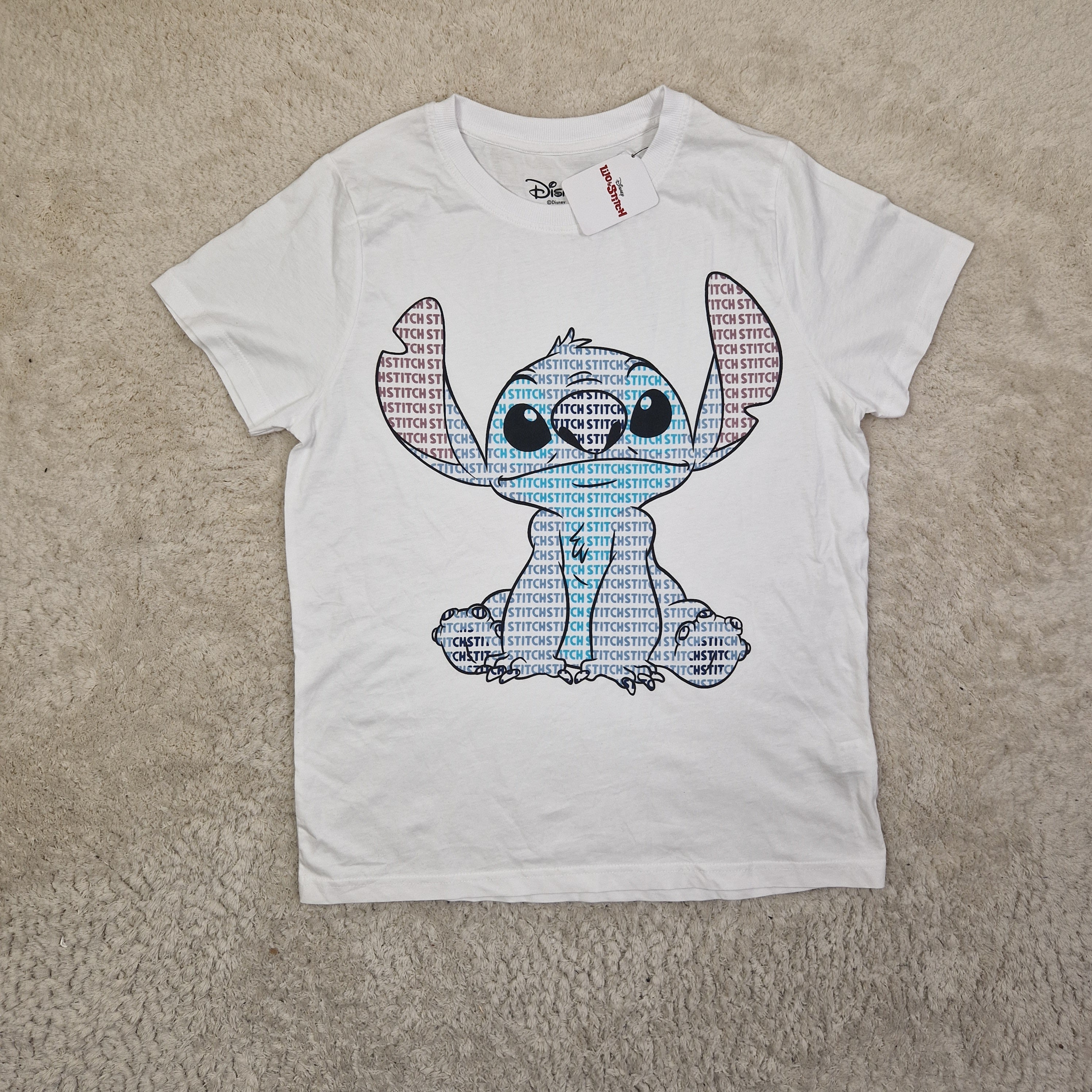 White t-shirt with a colorful fish graphic on a beige carpet