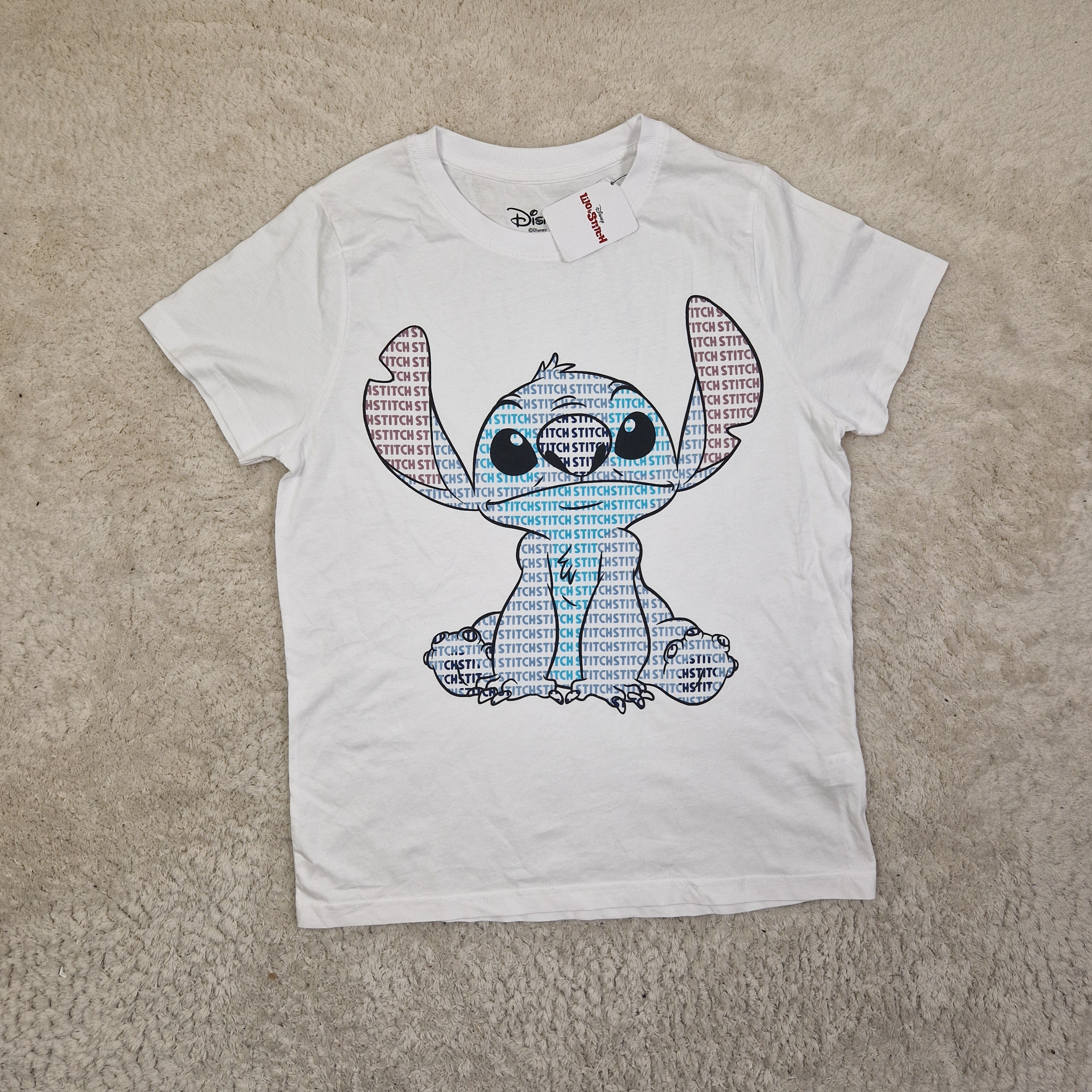 White t-shirt with a graphic design of a cartoon character on a beige carpet