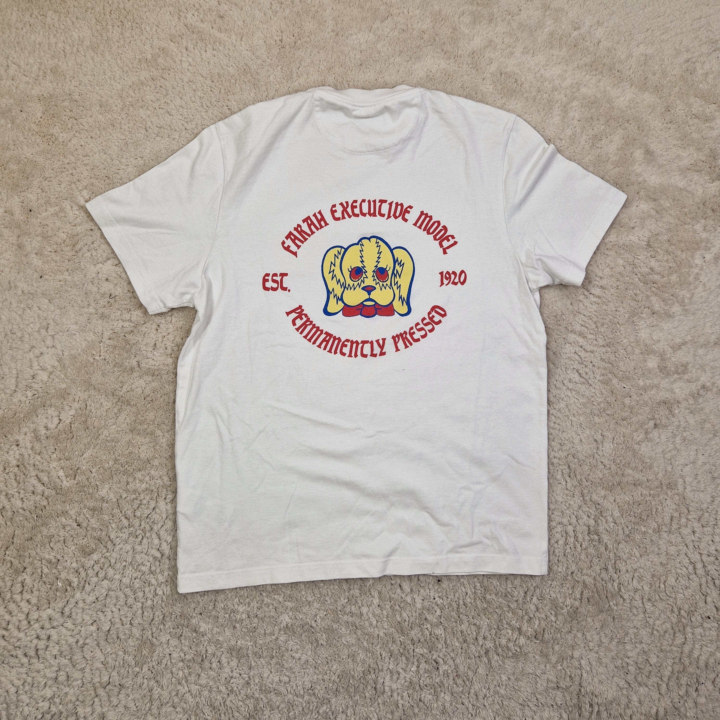 White long-sleeve shirt with a logo and text on a beige carpet