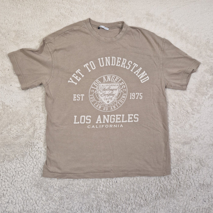Brown t-shirt with white text and graphics on a light gray carpet