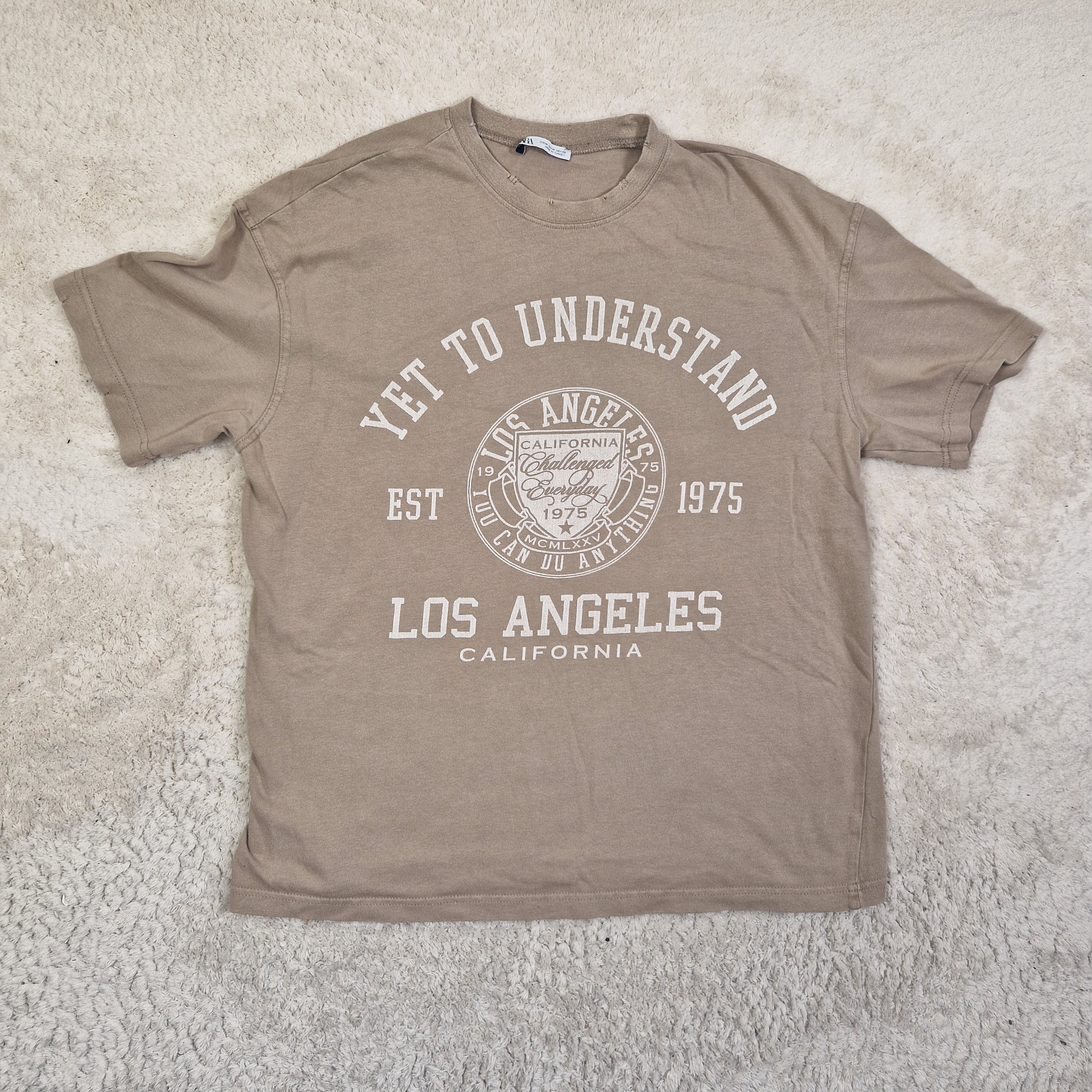 Brown t-shirt with white text and graphics on a light gray surface