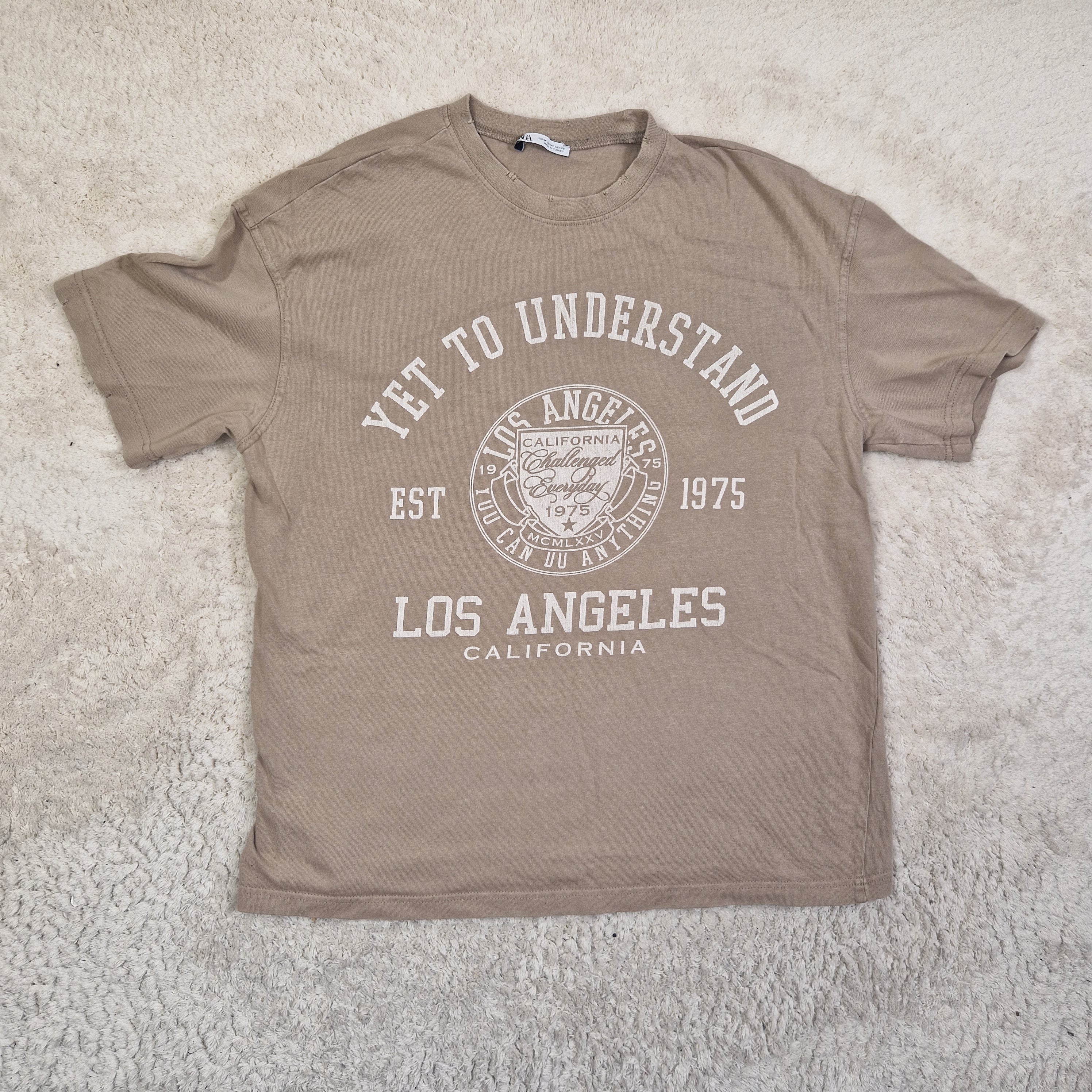 Brown t-shirt with white text and logo on a textured surface