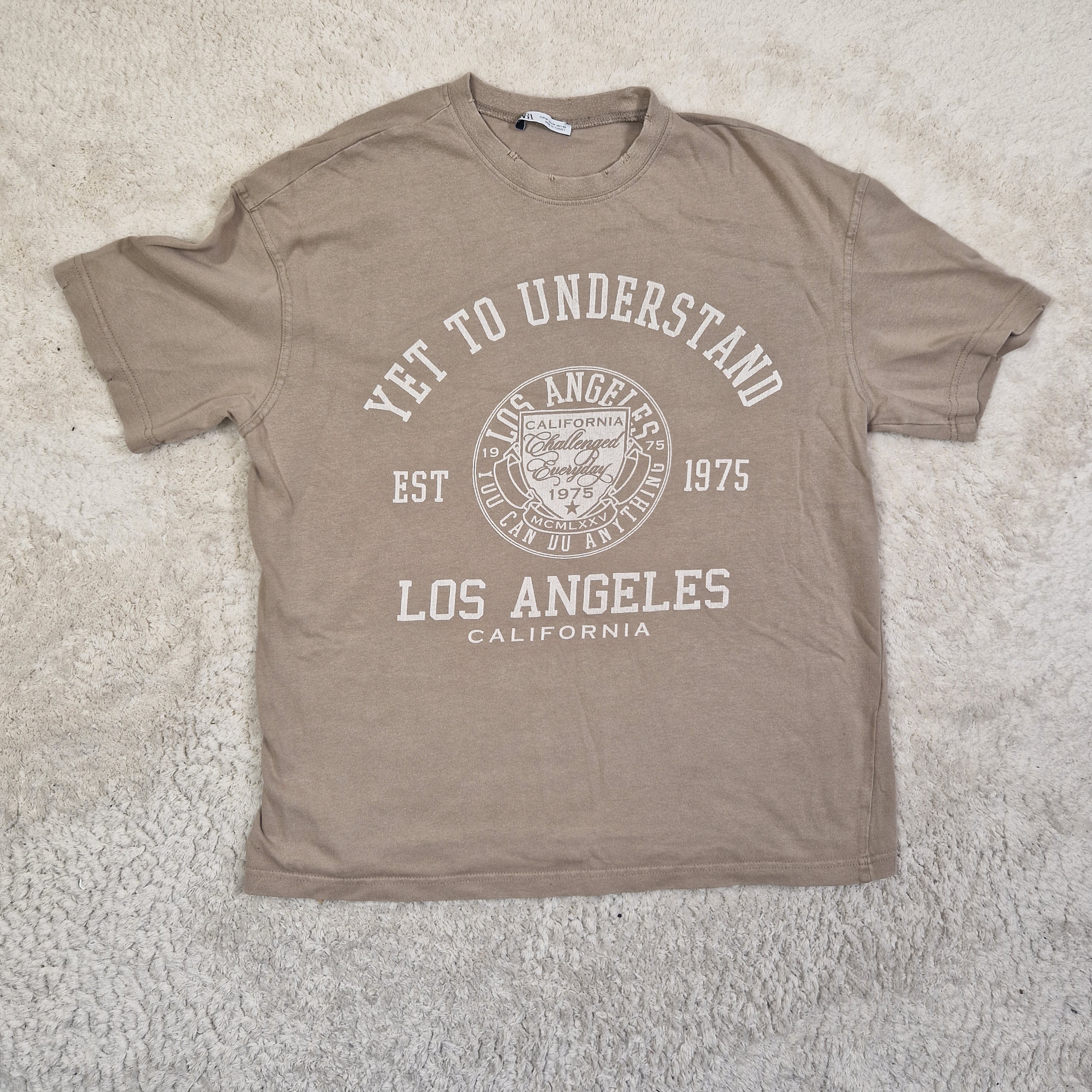 Brown t-shirt with white text and logo on a light gray surface