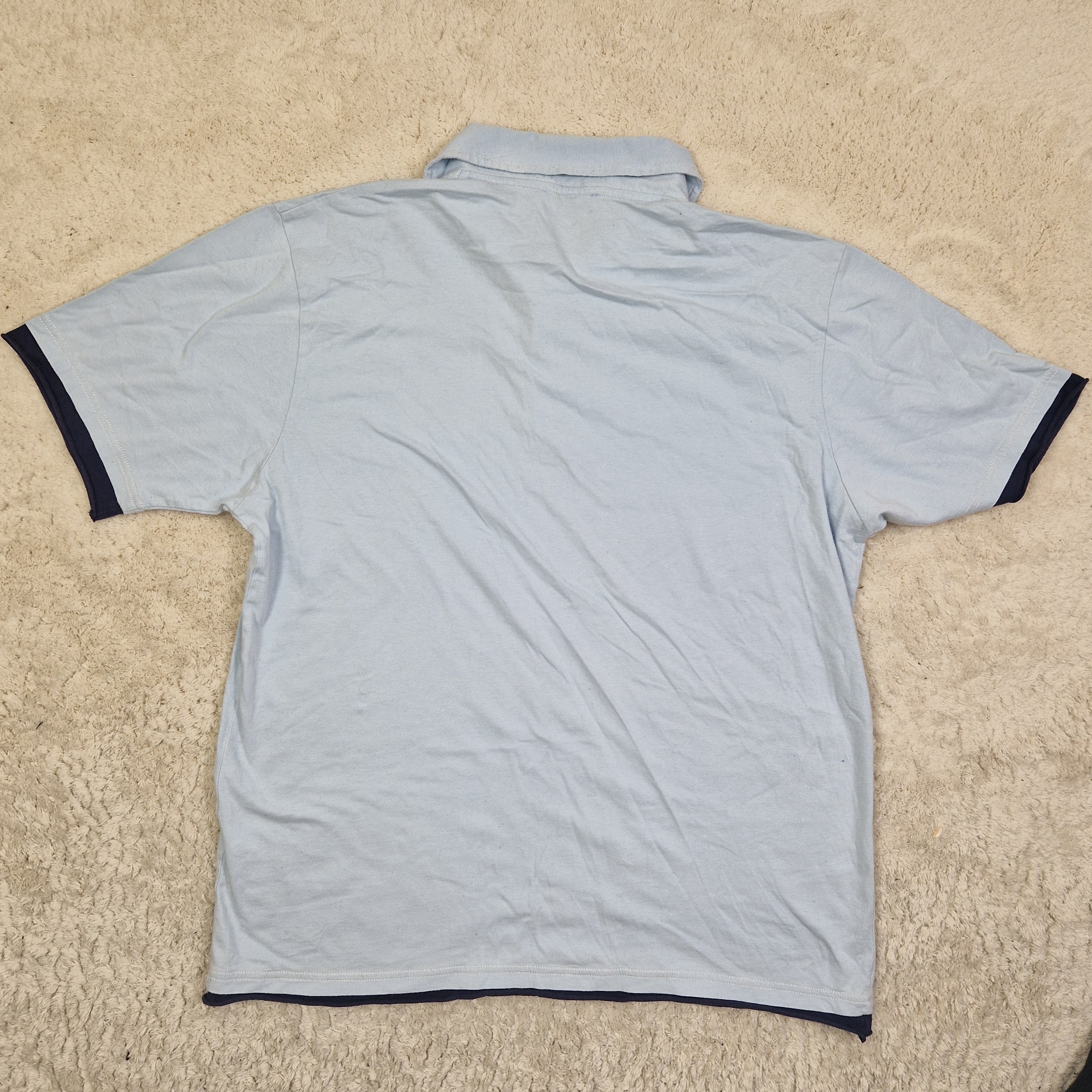 Light blue t-shirt with black trim on a beige carpet