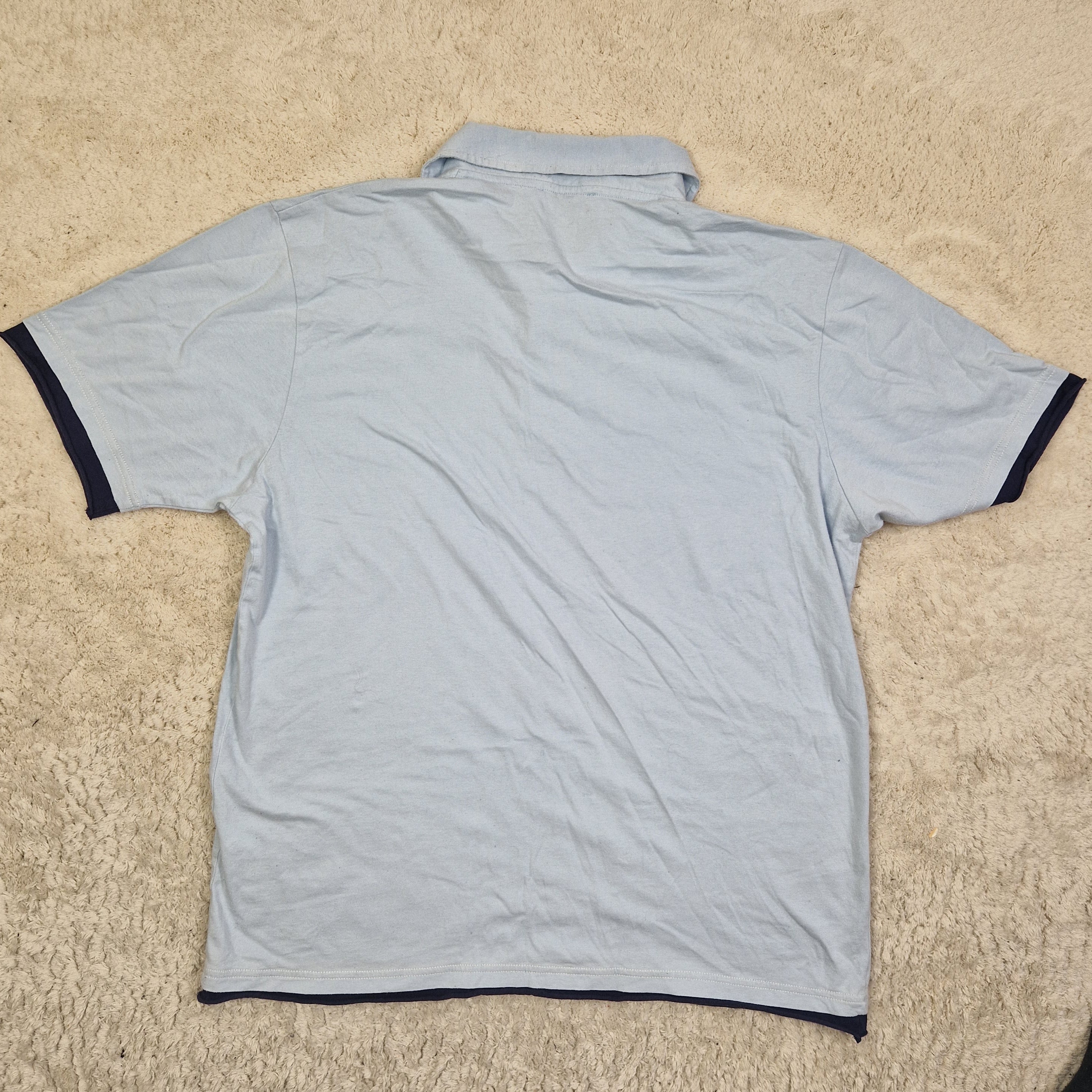 Light blue t-shirt with black trim on a beige carpet