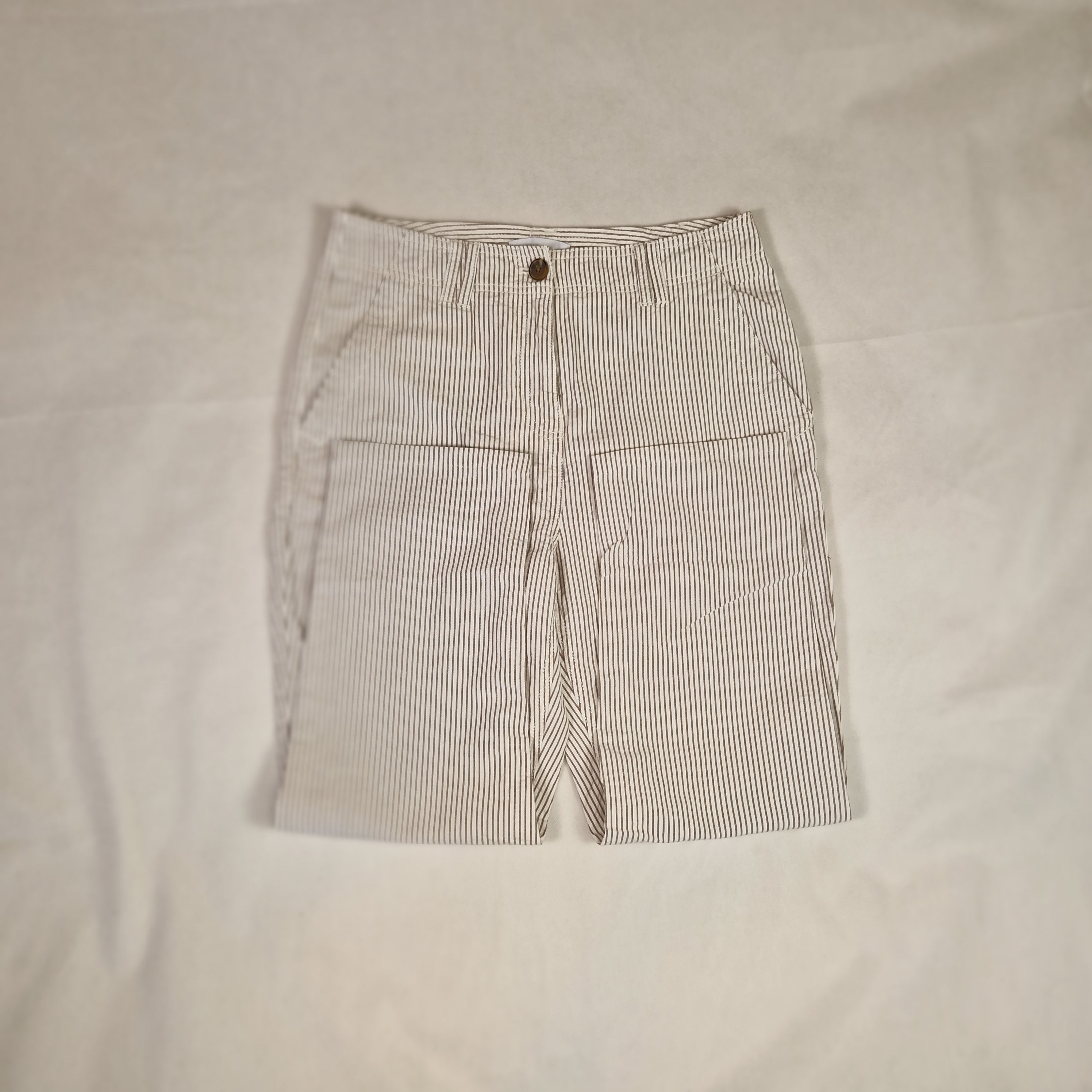 Folded beige shorts with a small button on a light beige background