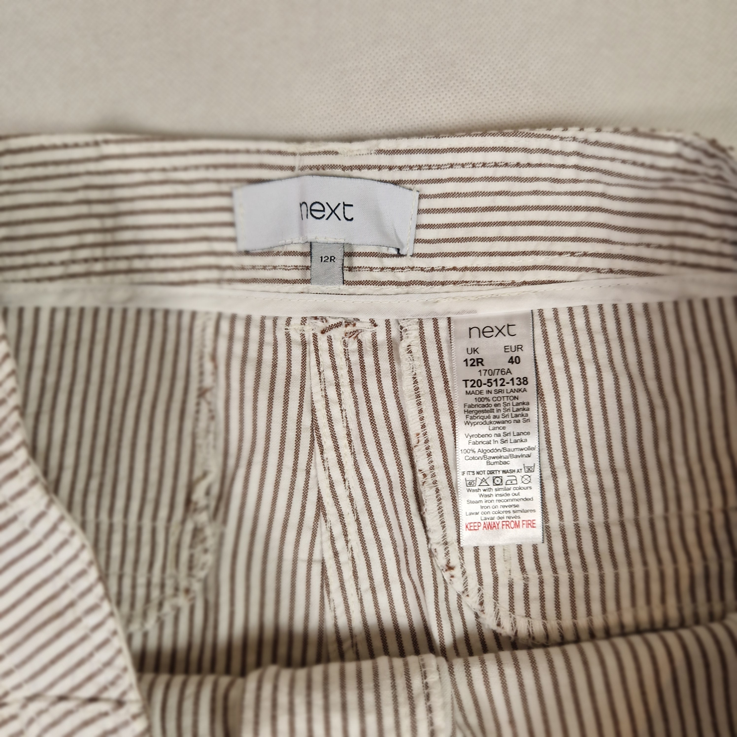 Close-up of a striped fabric with 'next' brand labels on a beige background