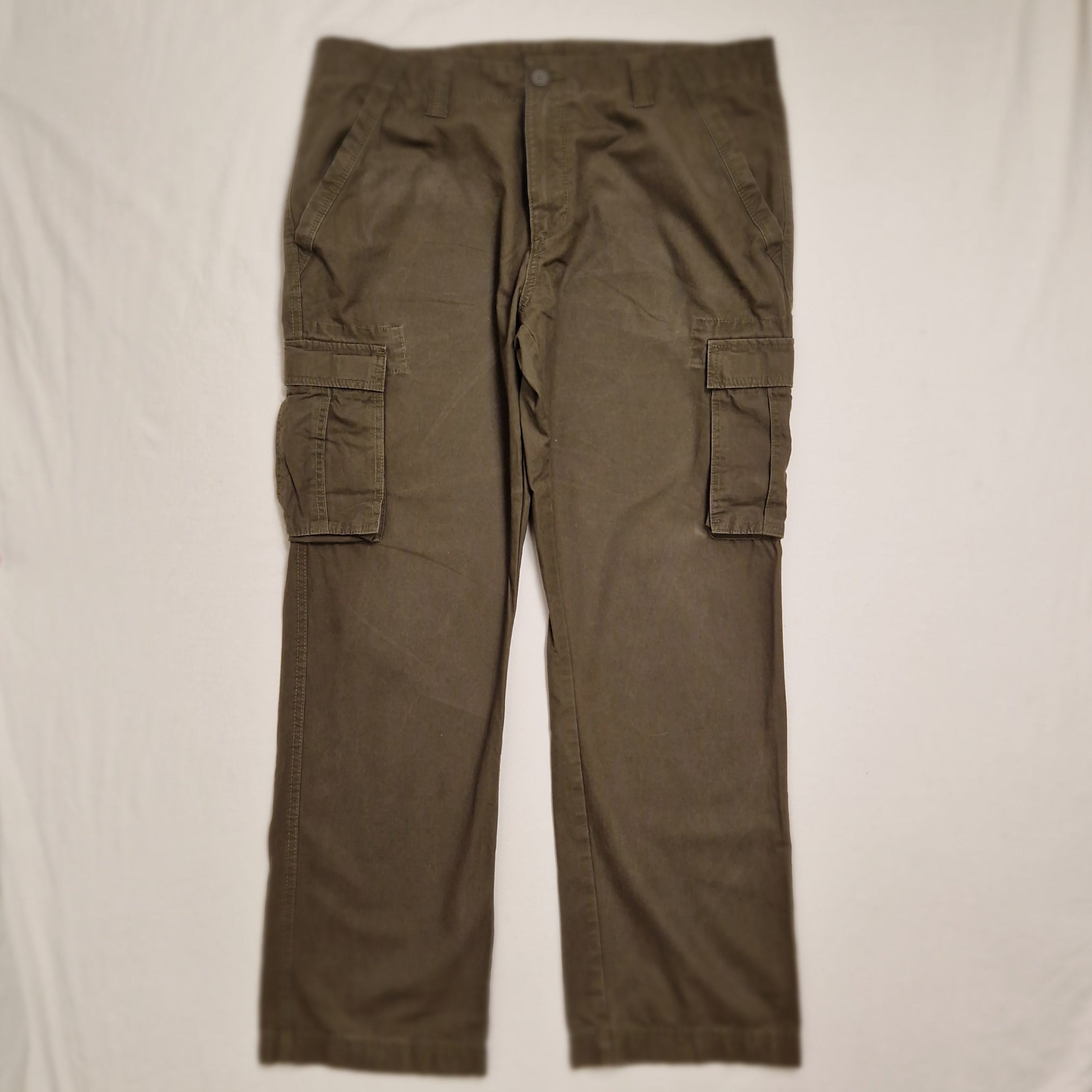 A pair of olive green cargo pants laid flat on a white fabric surface.