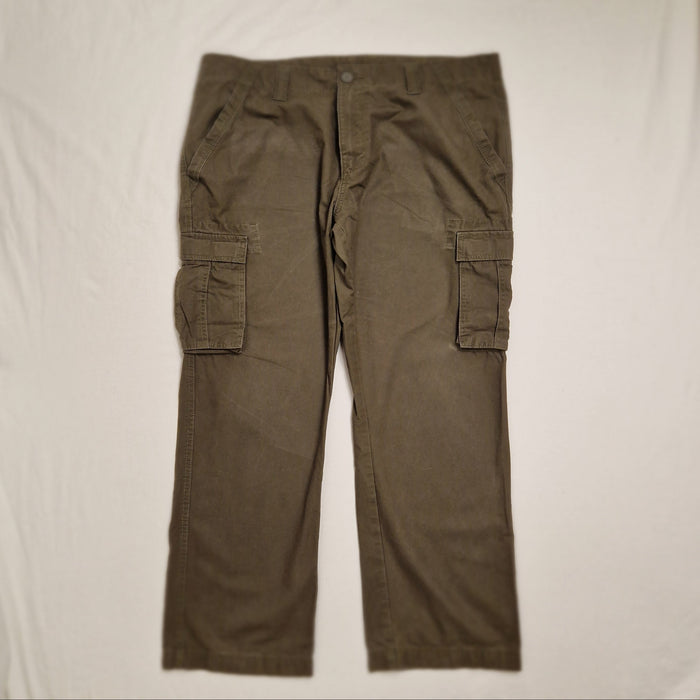 A pair of olive green cargo pants laid flat on a white fabric background, featuring side cargo pockets and a button fly.