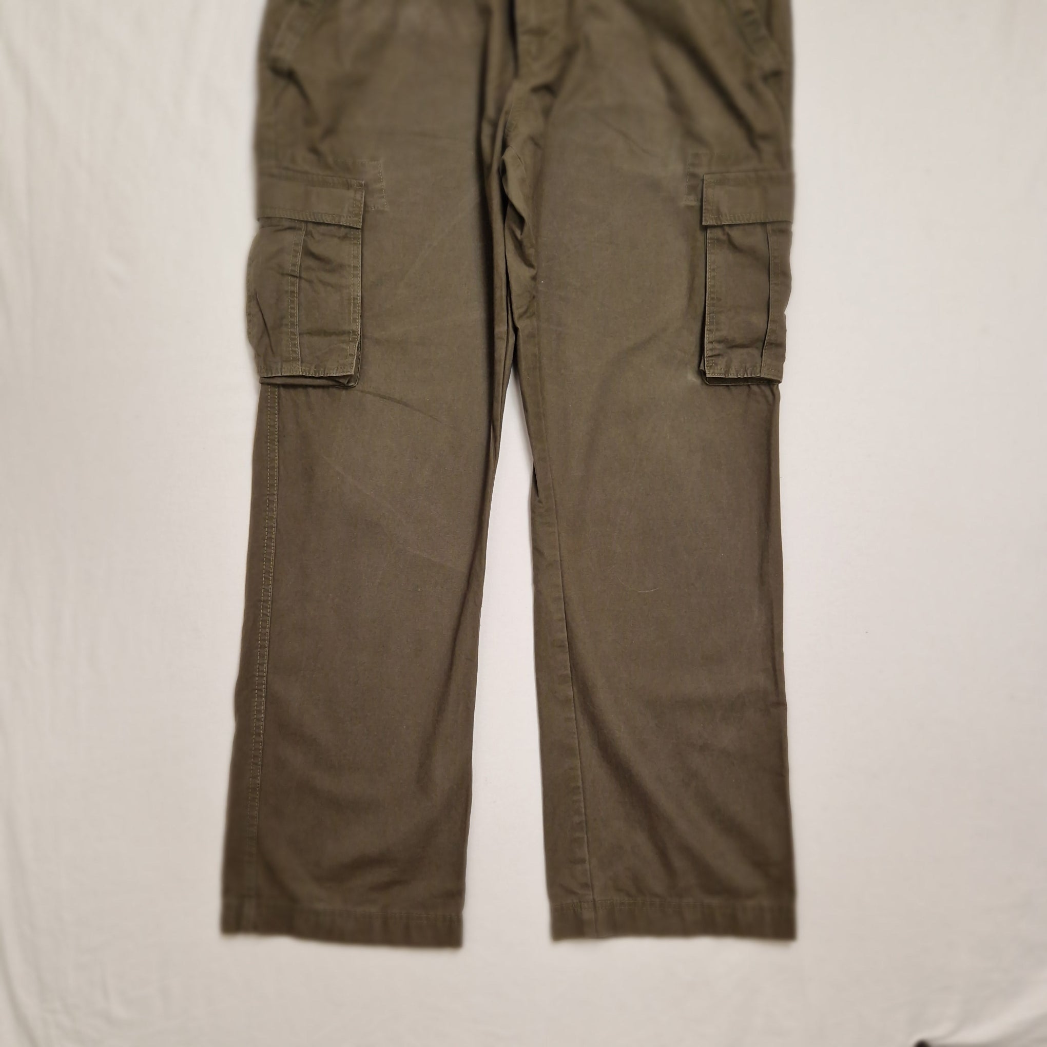 A pair of olive green cargo pants laid flat on a white fabric surface, showing the legs and side cargo pockets.