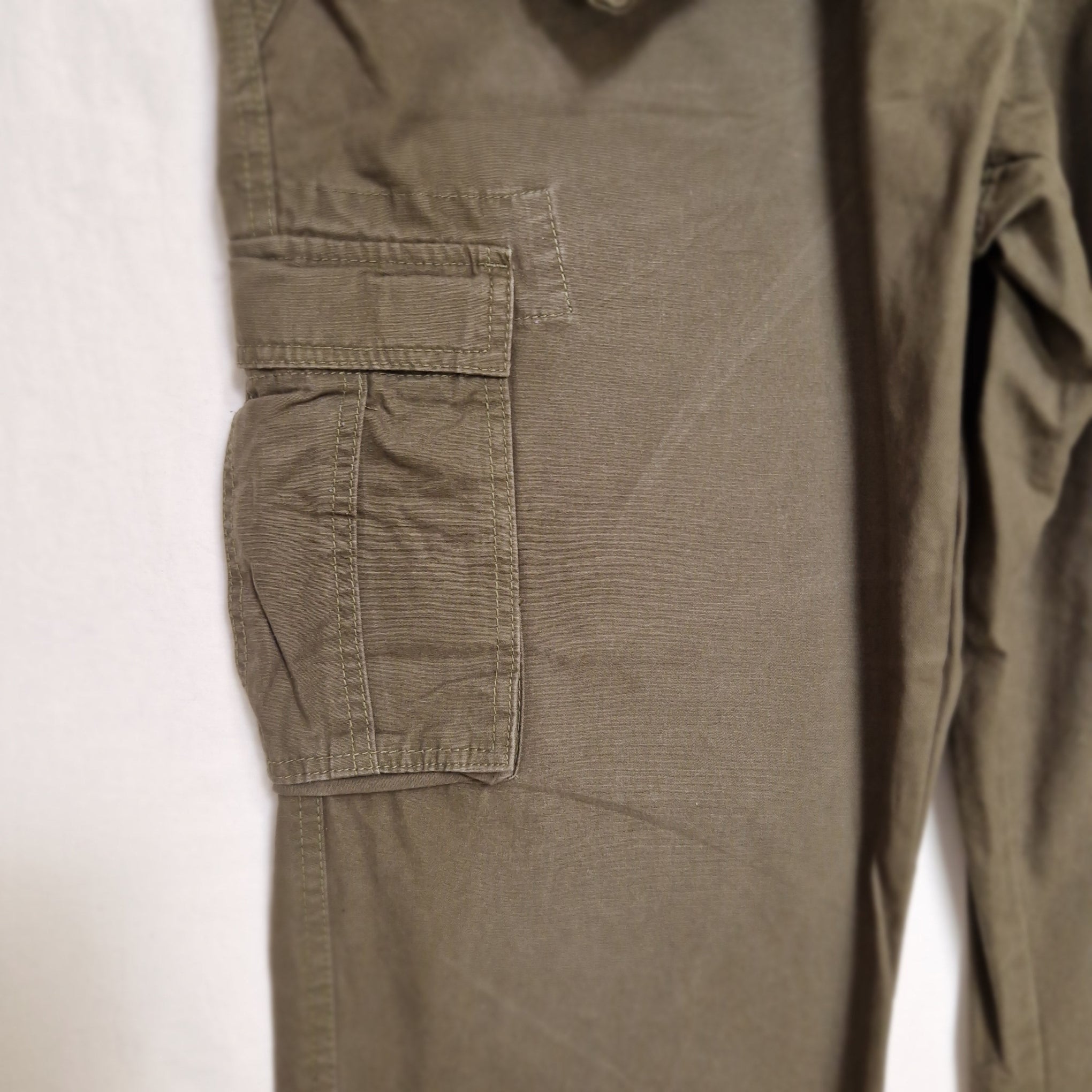 Close-up of olive green pants fabric with a front cargo pocket, laid flat on a white surface.