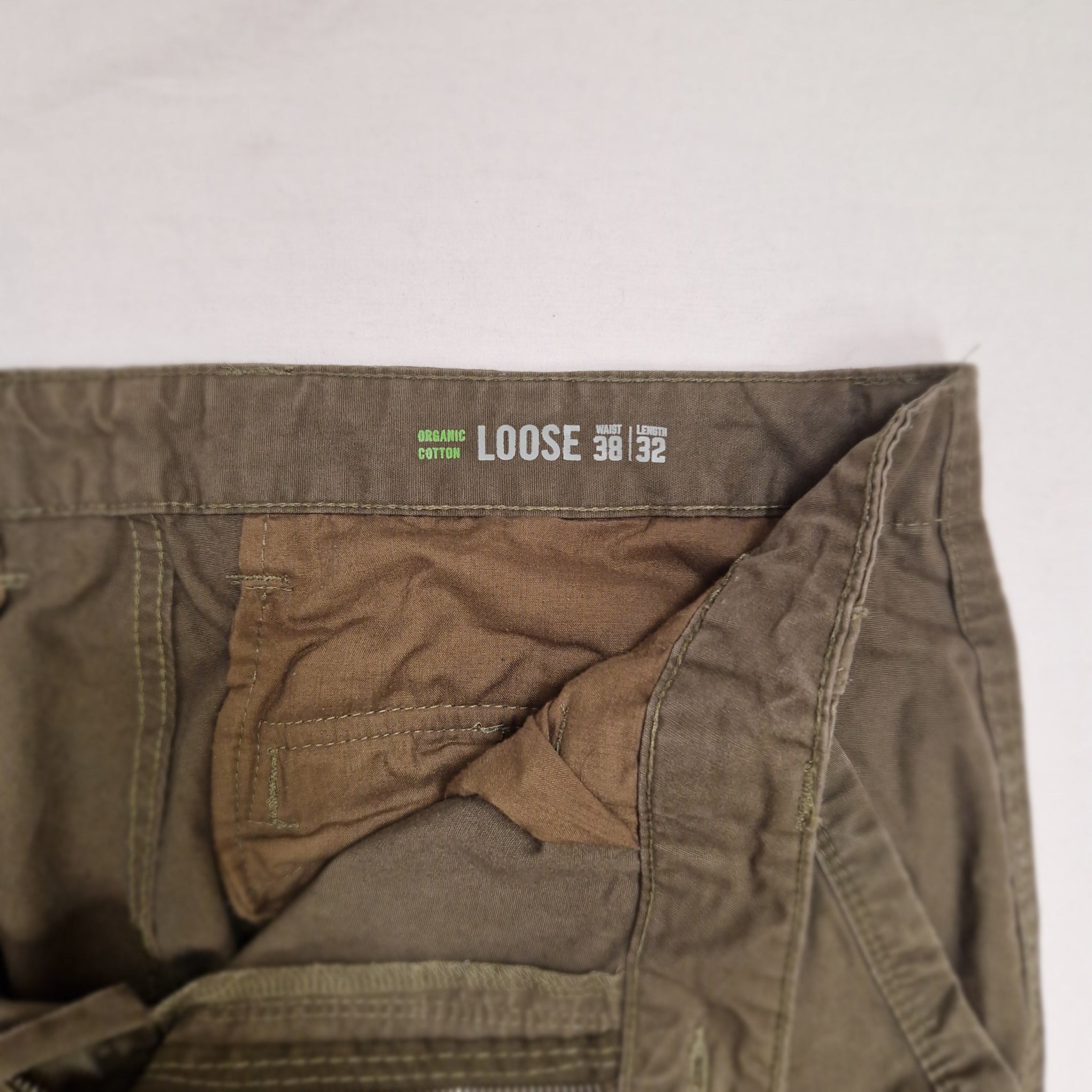 Close-up of the waistband and inner pocket area of loose-fit cargo pants in an olive drab color, with a brown inner lining and a waistband label reading 'LOOSE' and 'CLOTHING MFG'.