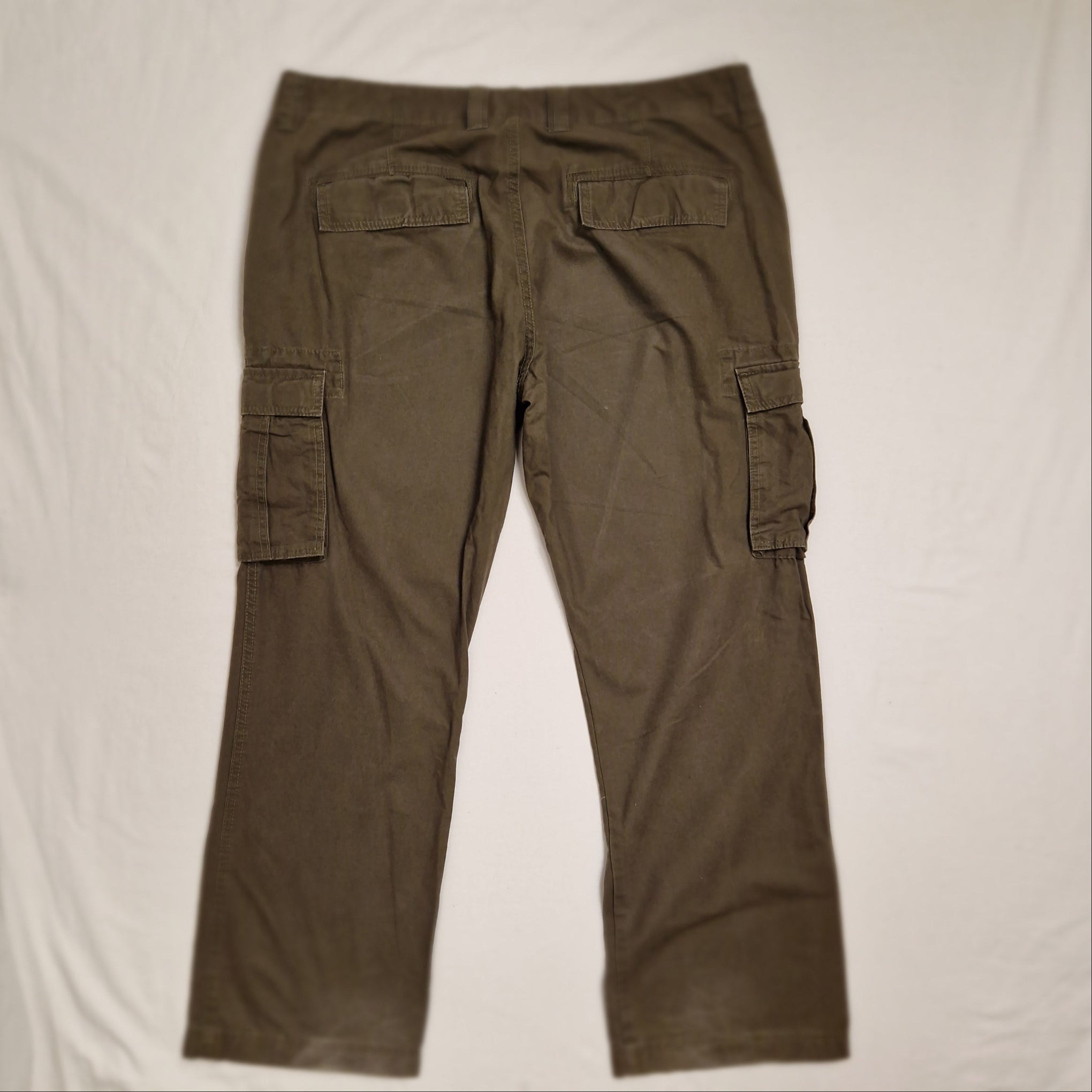 A pair of olive green cargo pants laid flat on a white fabric background.