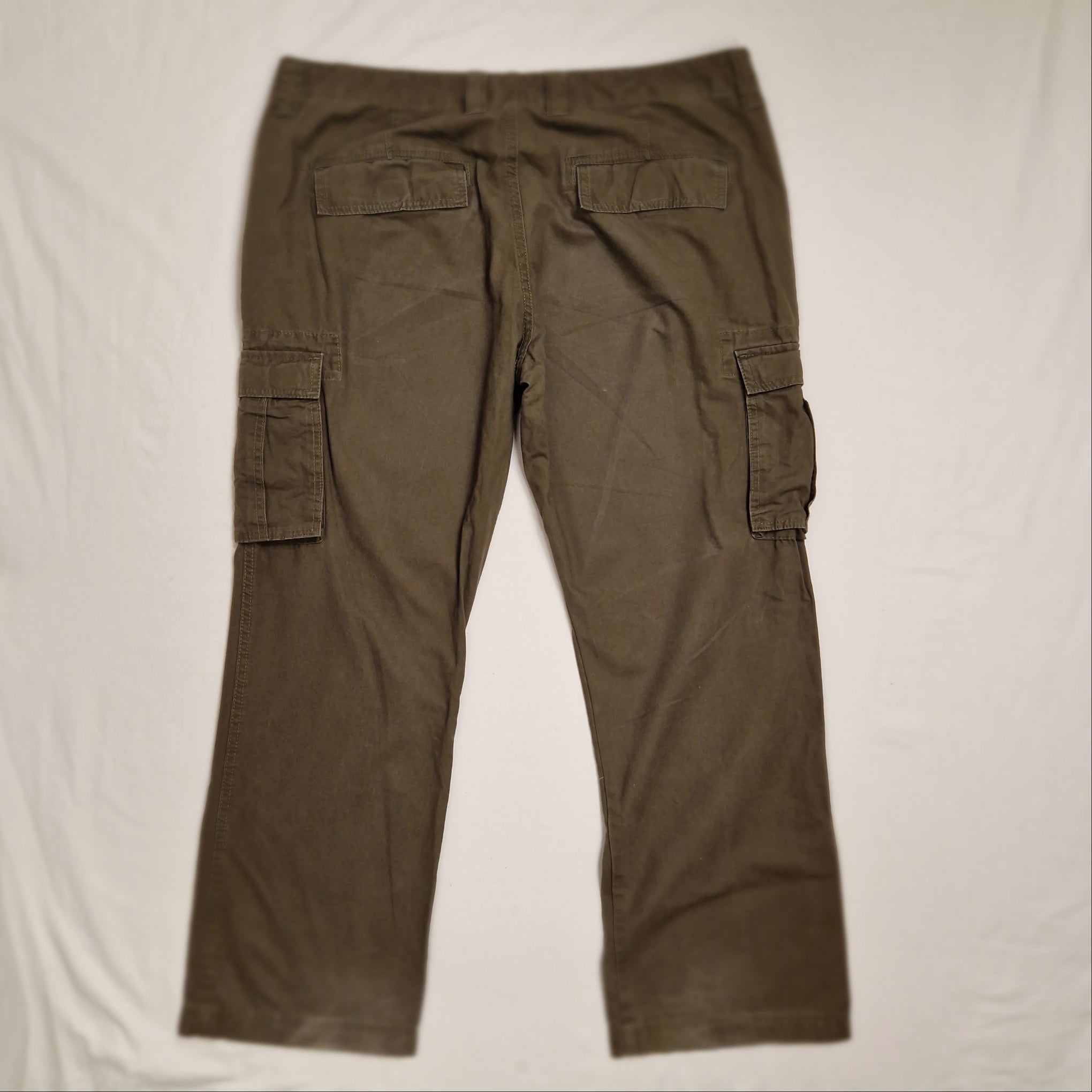 A pair of olive brown cargo pants laid flat on a white sheet, showing the front pockets and leg structure.