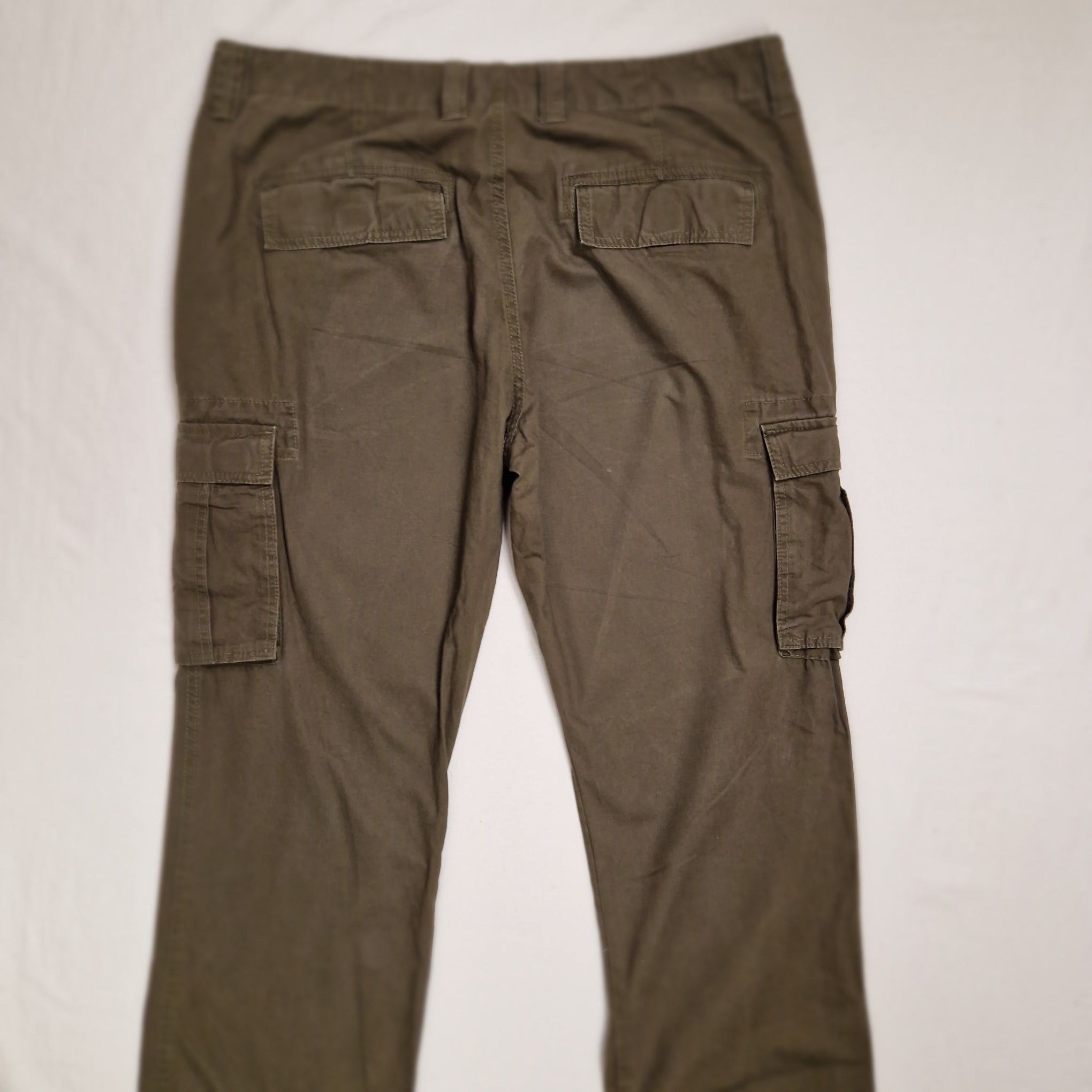 A pair of olive green cargo pants laid flat on a white fabric background, showing the lower half with cargo pockets on both legs.
