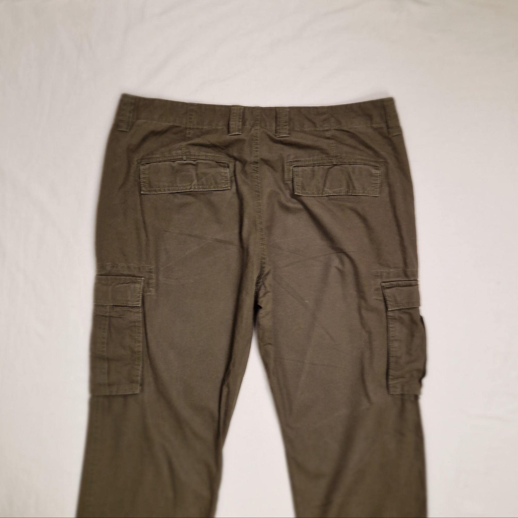 A pair of olive green cargo pants laid flat on a white fabric background, showing the back side with multiple cargo pockets.