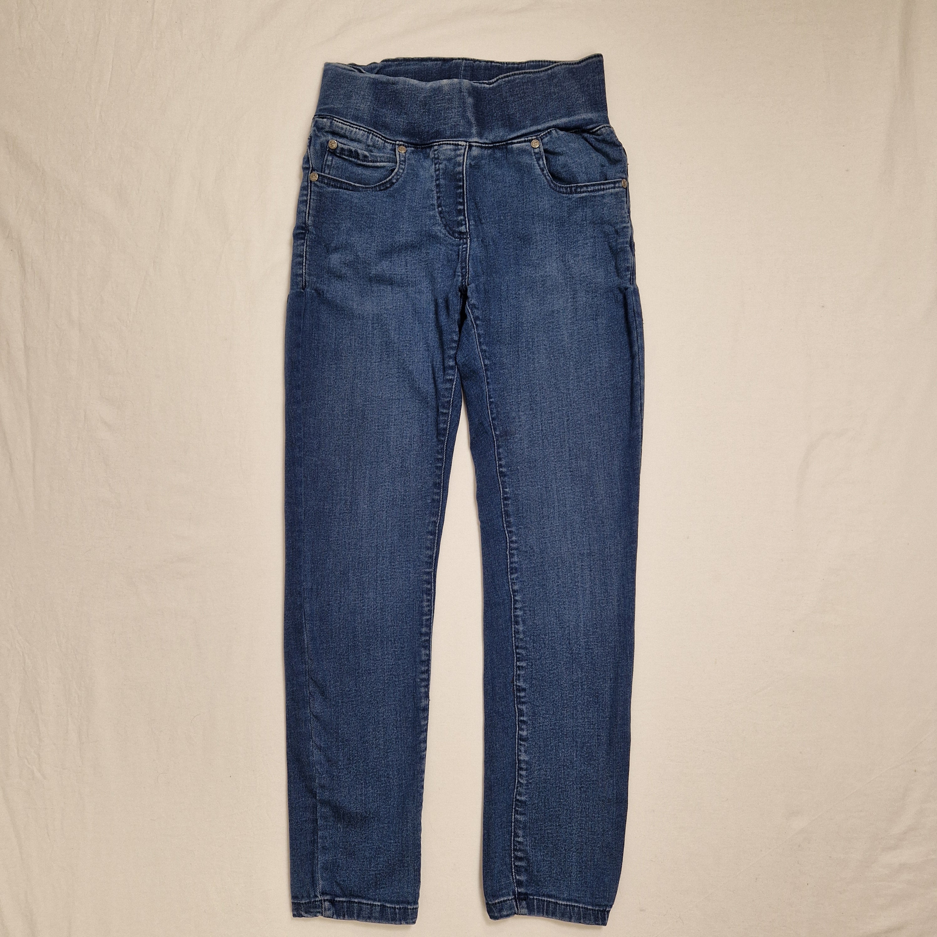 A pair of medium wash blue denim jeans laid flat on a light beige fabric background.