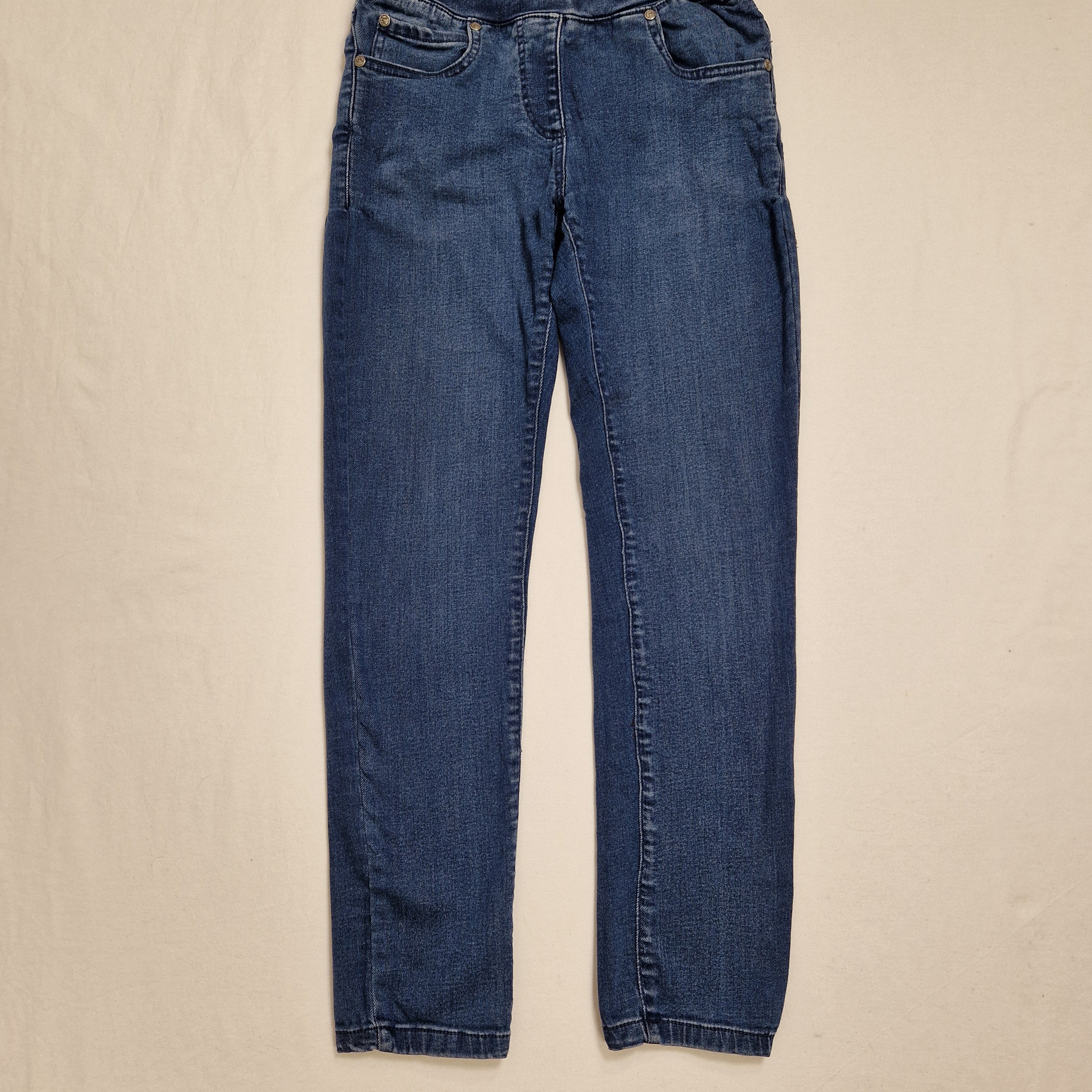 A pair of medium wash blue denim jeans laid flat on a light beige fabric background.